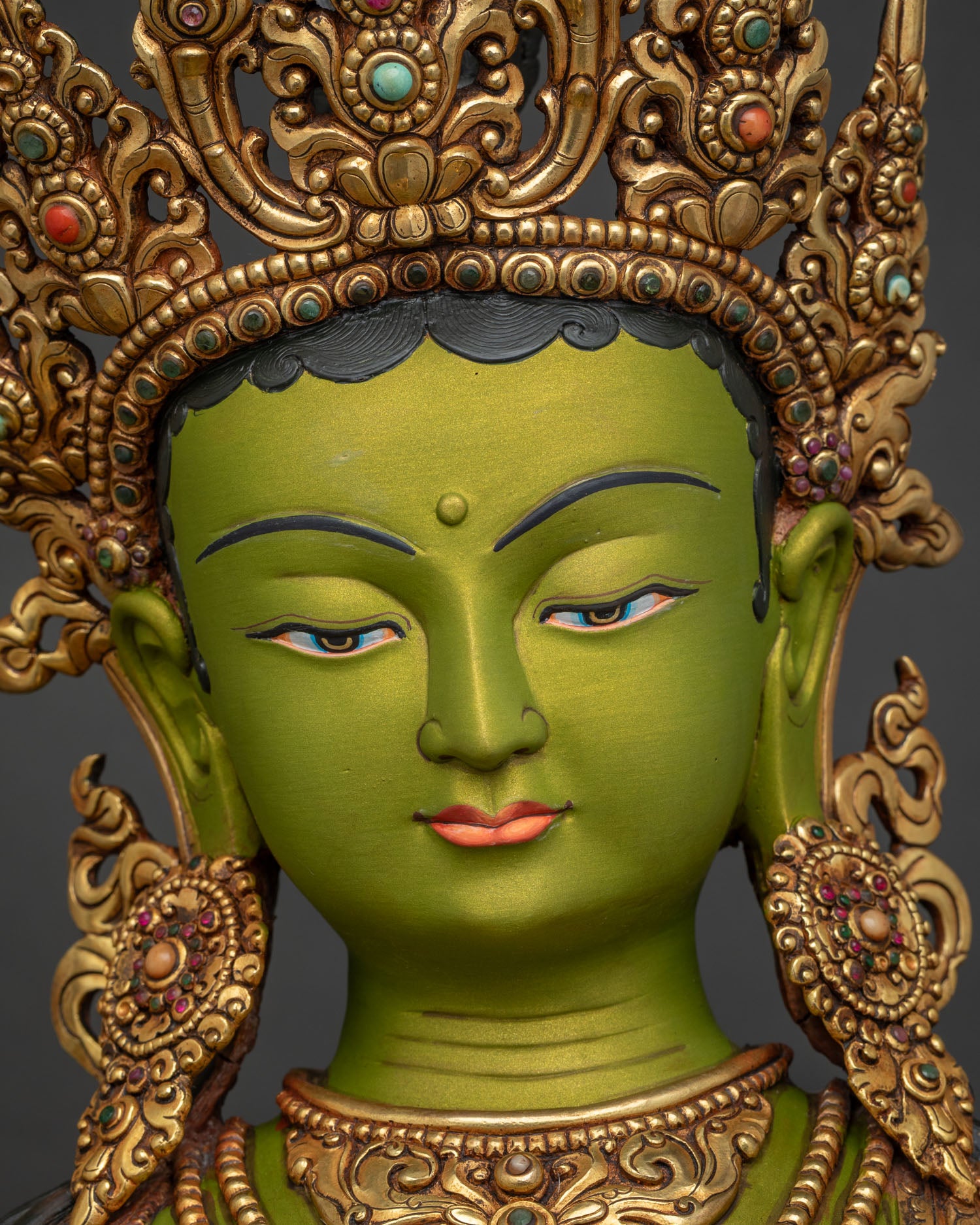 Detailed close up face of Green Tara statue with serene expression and jeweled crown