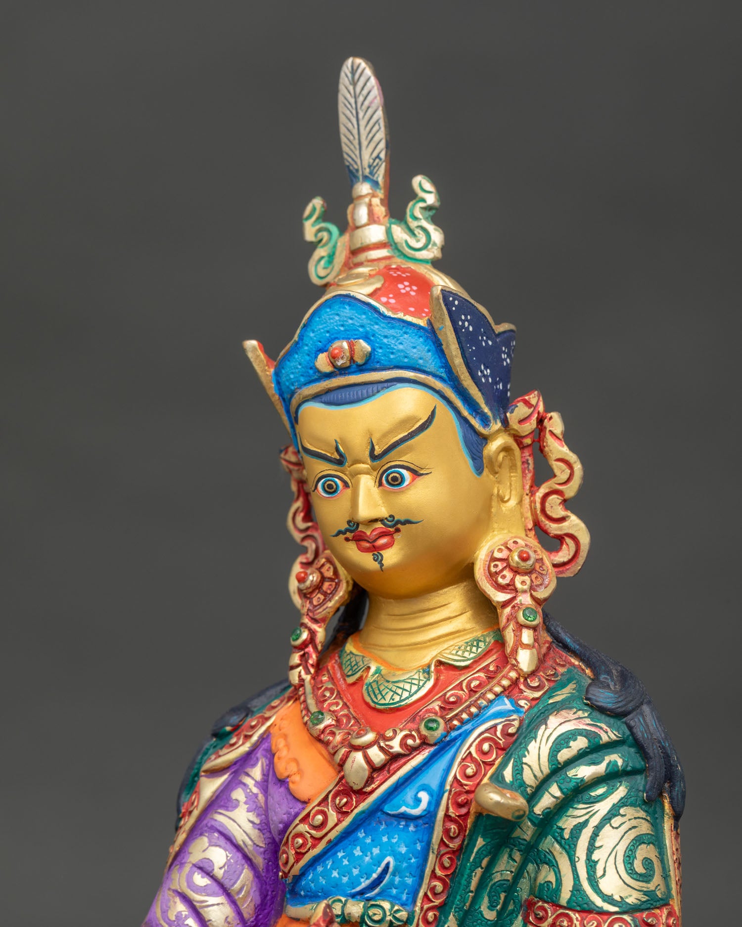 Detailed close up Guru Rinpoche face with radiant gold paint and carved floral motifs.
