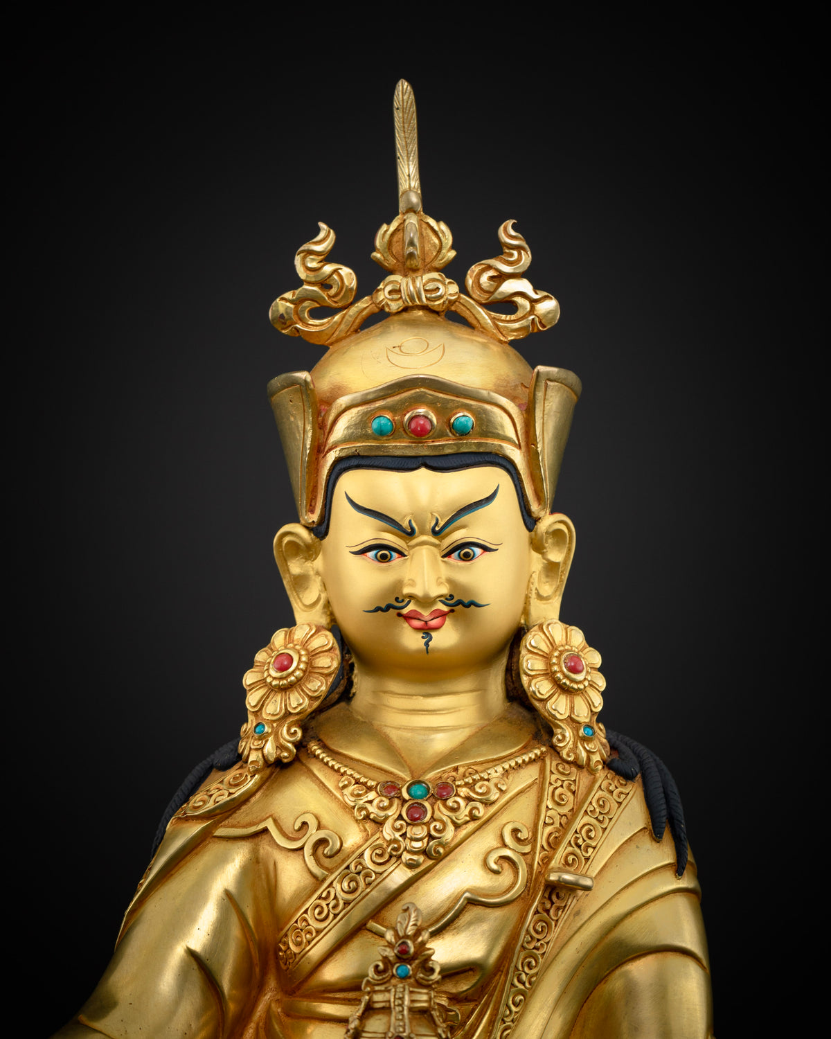 Detailed close up of Guru Rinpoche luminous 24K gold-painted face with semi-wrathful expression