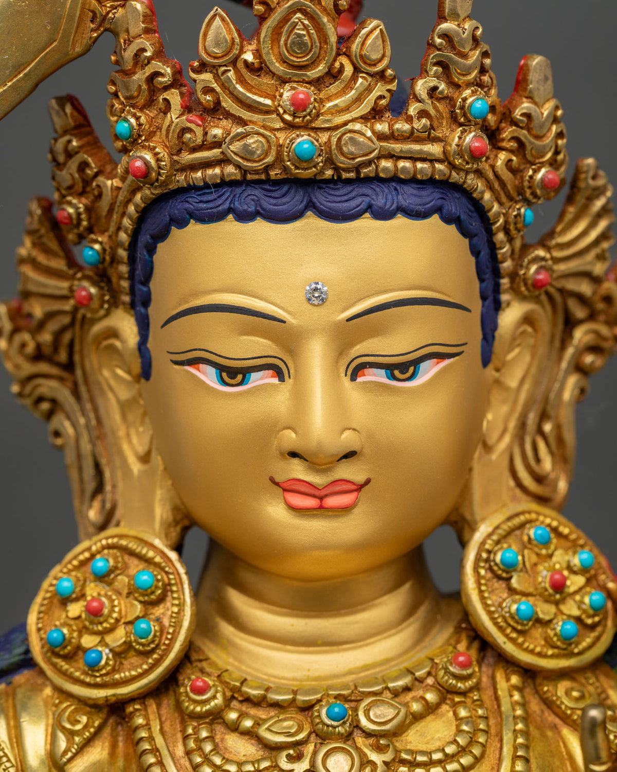 Detailed close up of Maha Manjushri statue face with serene expression and gold painted features