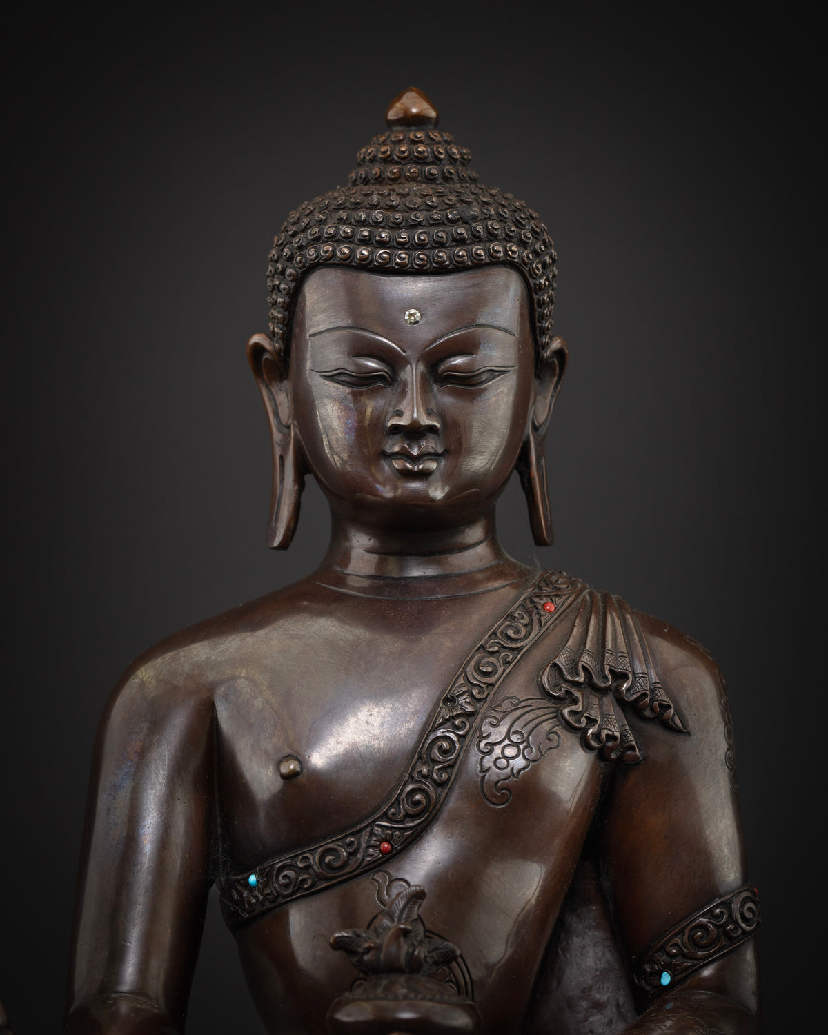 Detailed close up of Medicine Buddha face, serene expression on oxidized copper Nepalese statue