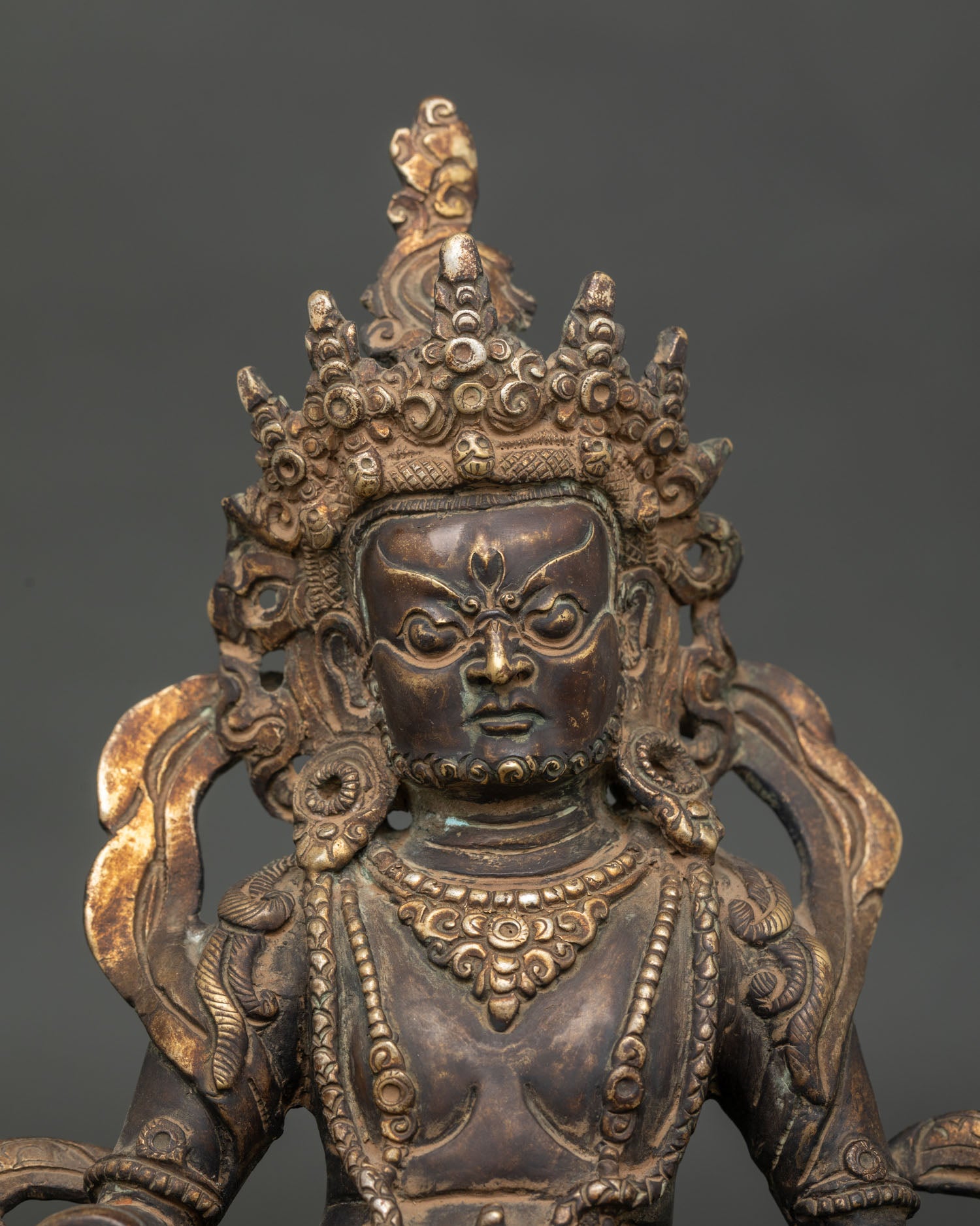 Detailed Dzambhala statue face with five jewel crown flowing scarf and royal garments.