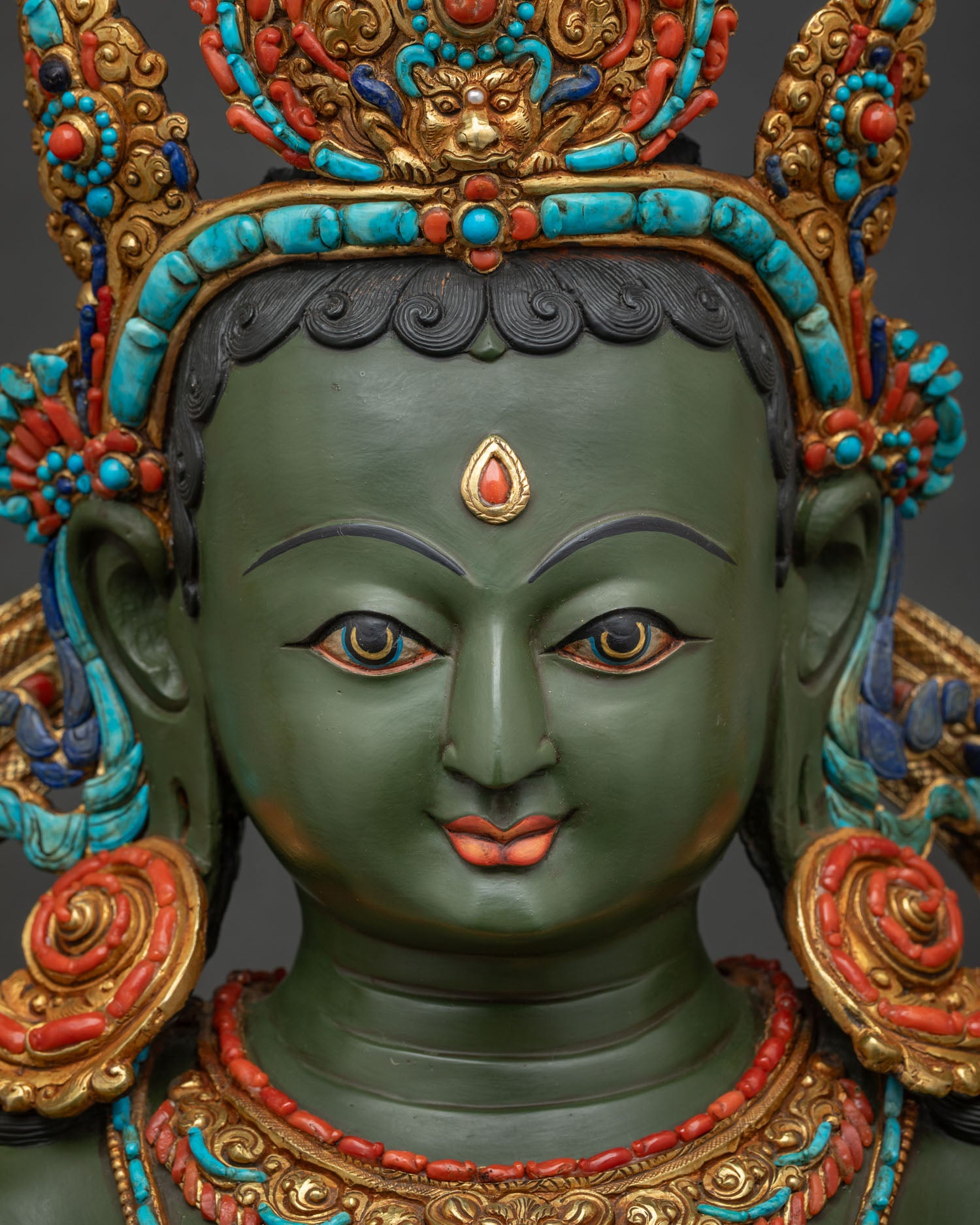 Detailed face of Green Tara statue showing serene expression hand painted details and gemstone crown.