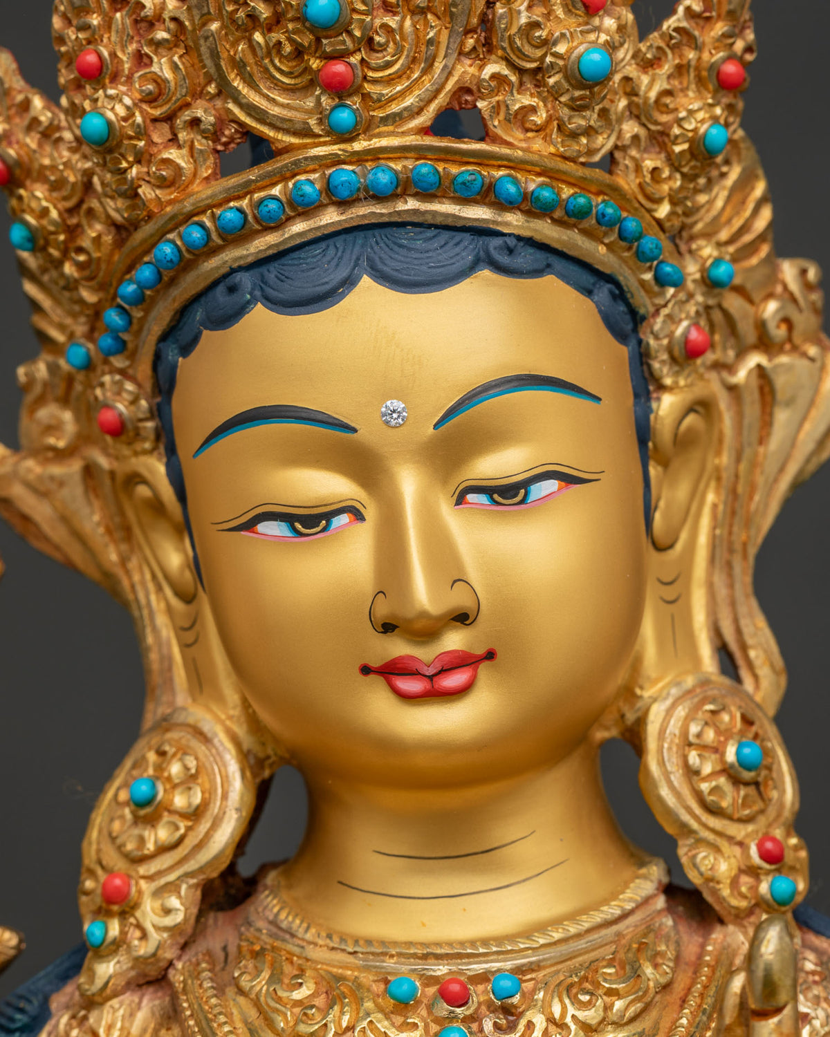 Detailed face of Green Tara statue with serene gold-painted features and hand-set turquoise stonesa