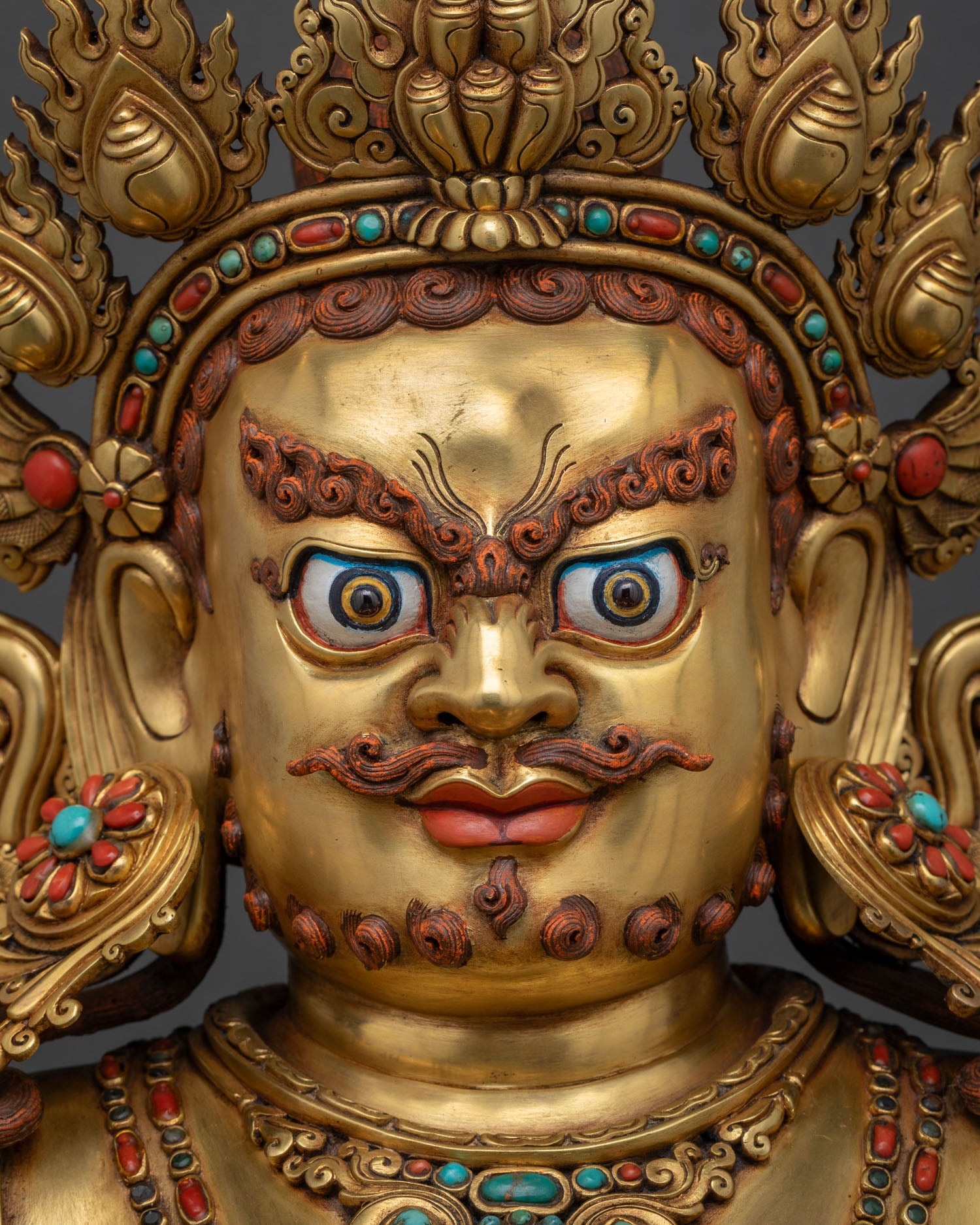 Detailed facial close-up of Dzambhala statue with painted eyes and 5-jeweled crown.