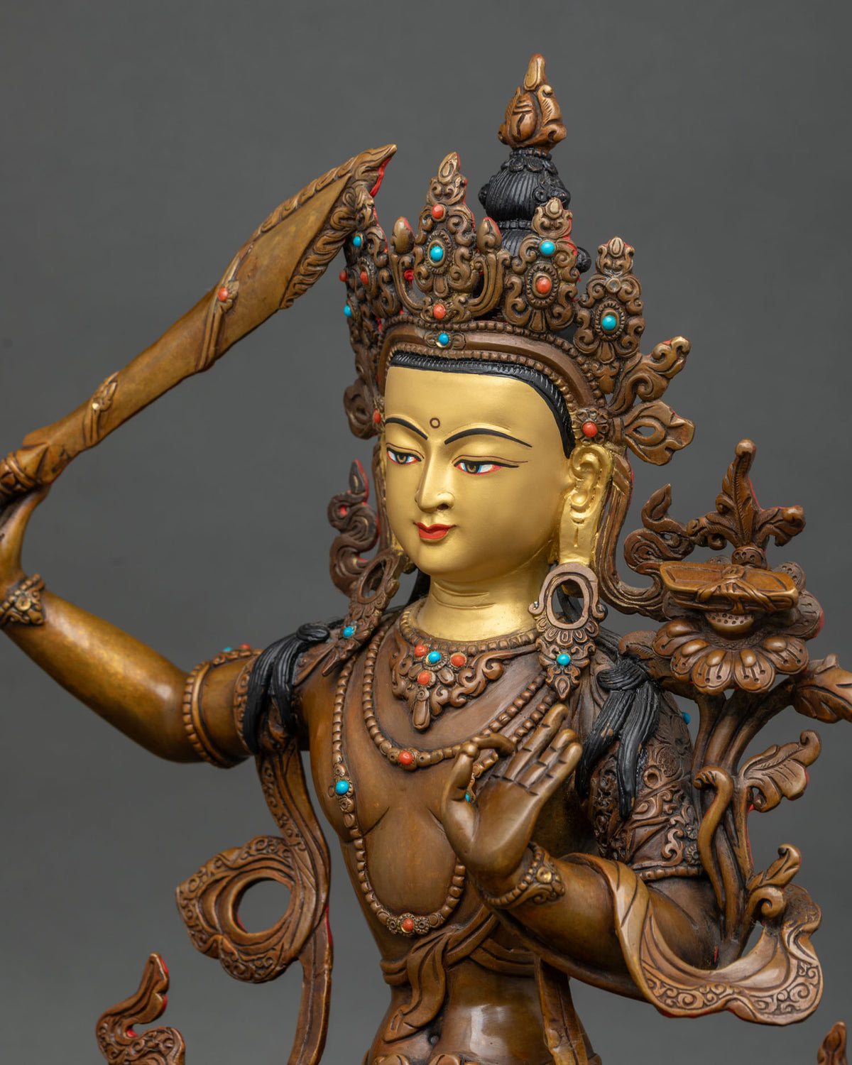 Detailed side close up of oxidized copper Manjushri statue with turquoise and coral stones