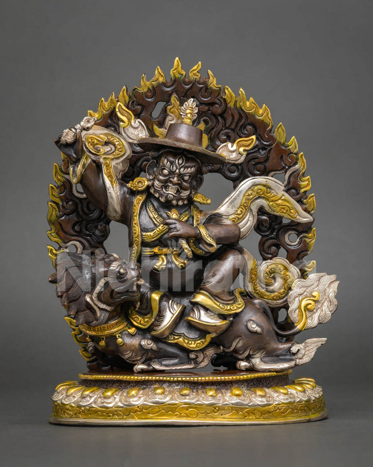 Dorje Legpa statue seated on a snow lion with flame halo, gold and silver accents in oxidized copper