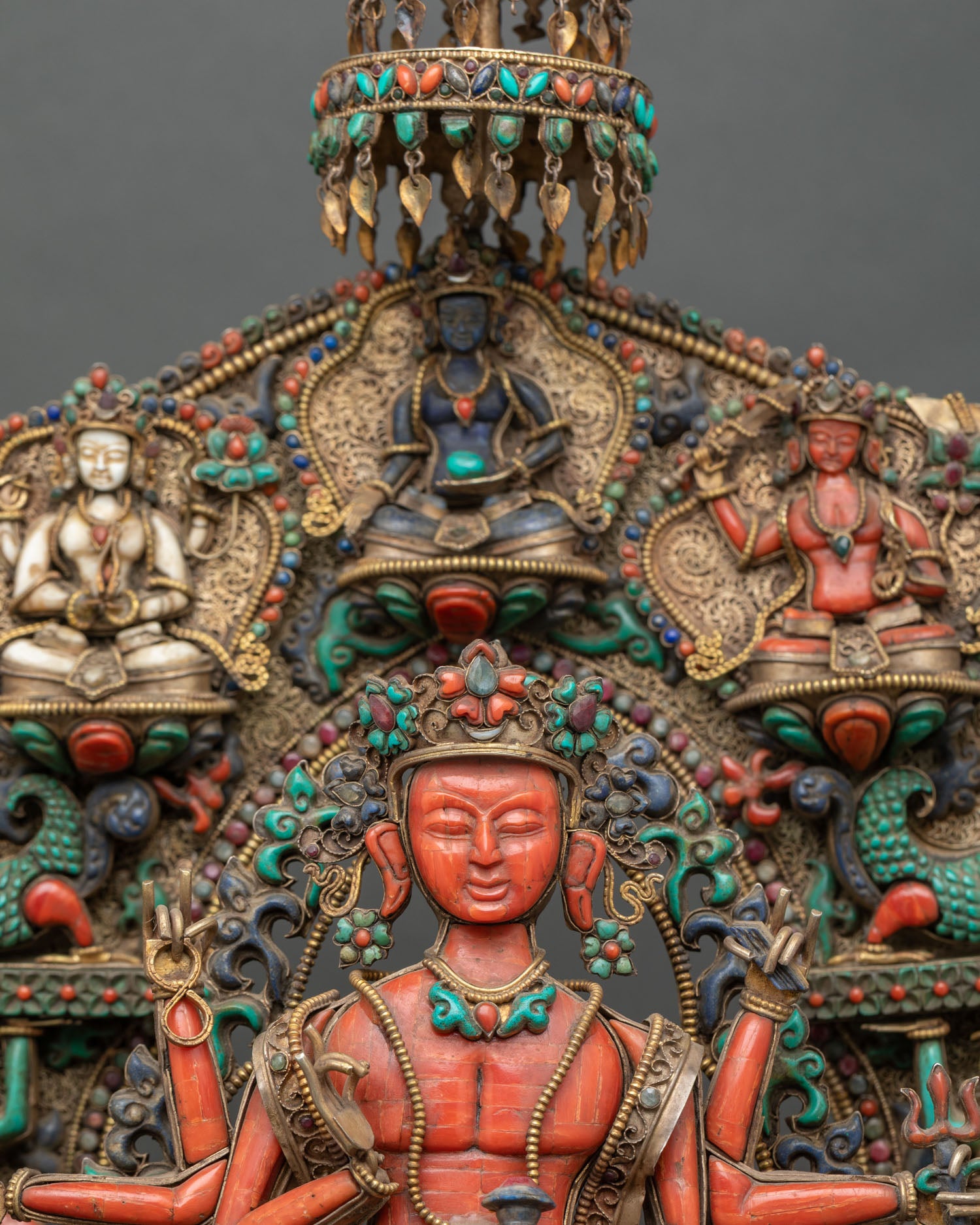 Face close-up of coral Chenrezig statue with serene expression, gold crown, and gemstone ornaments