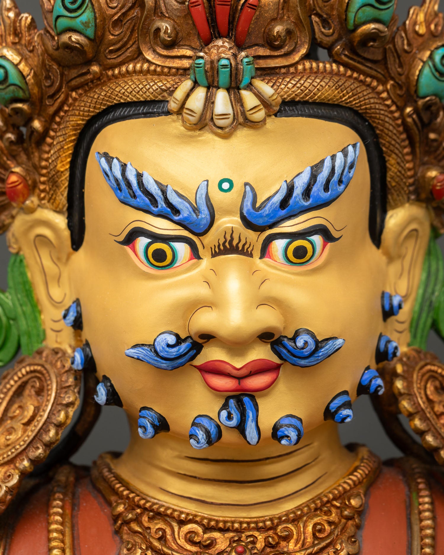 face close up of dzambhala buddhist deity with gold painted expression and piercing eyes