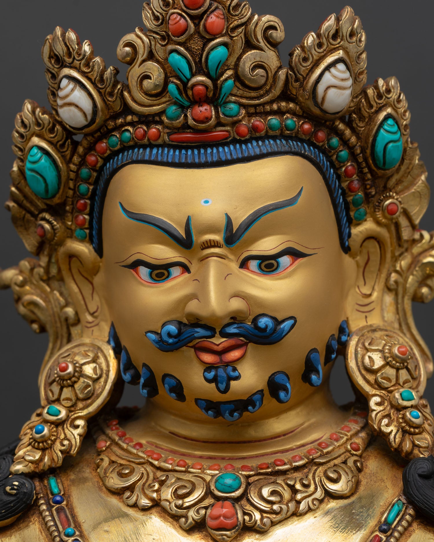 face close up of dzambhala statue, wrathful expression with gold gilded finish