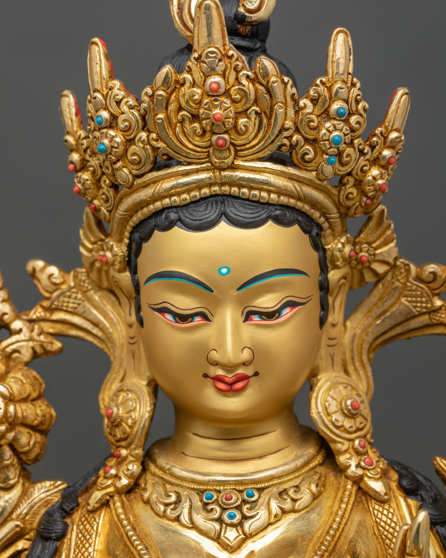 Face close-up of Green Tara statue with gold-painted features and serene expression