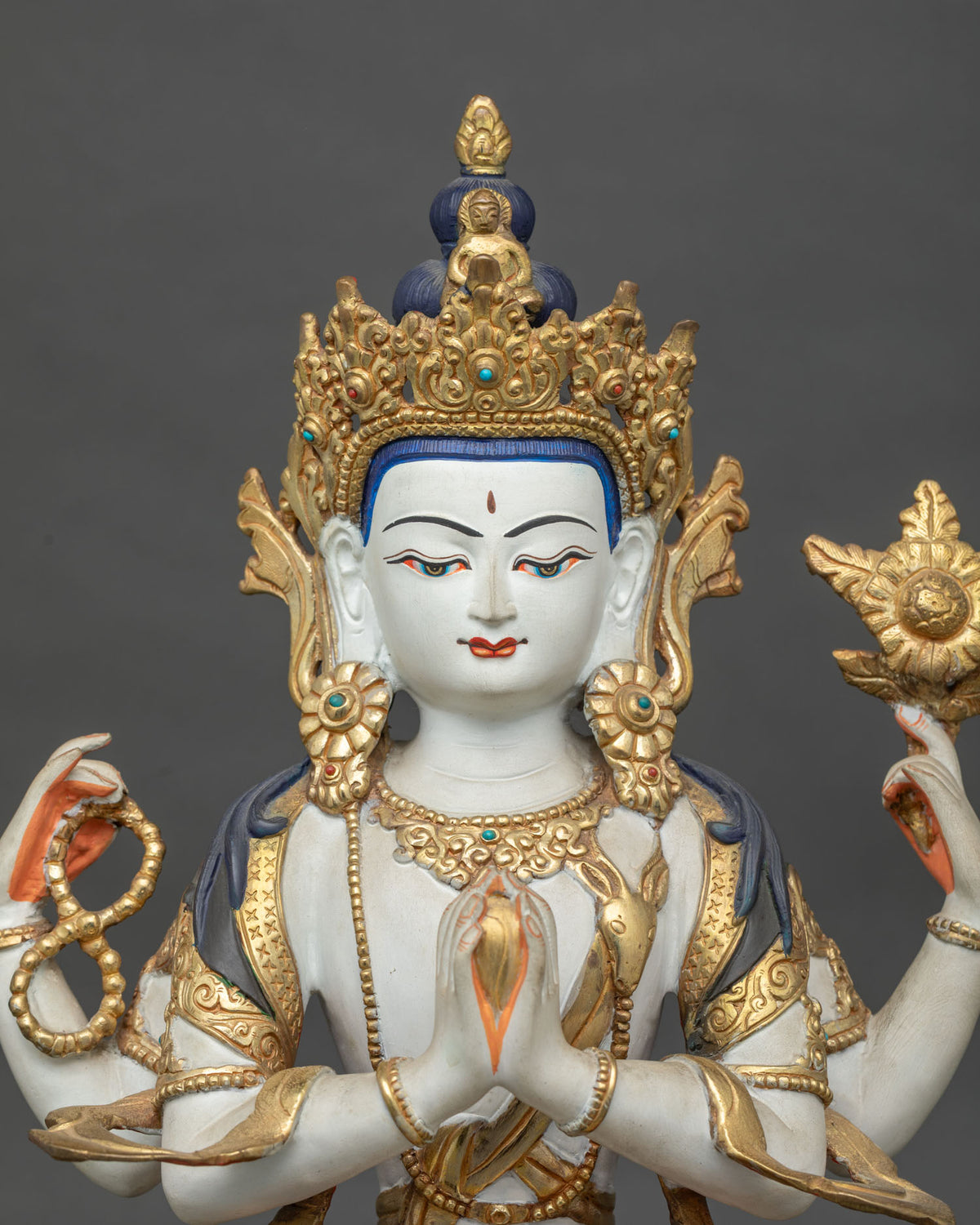 Close-up of four-armed Chenrezig statue featuring a serene face, acrylic colors, gold-gilded details, and traditional Nepalese craftsmanship.