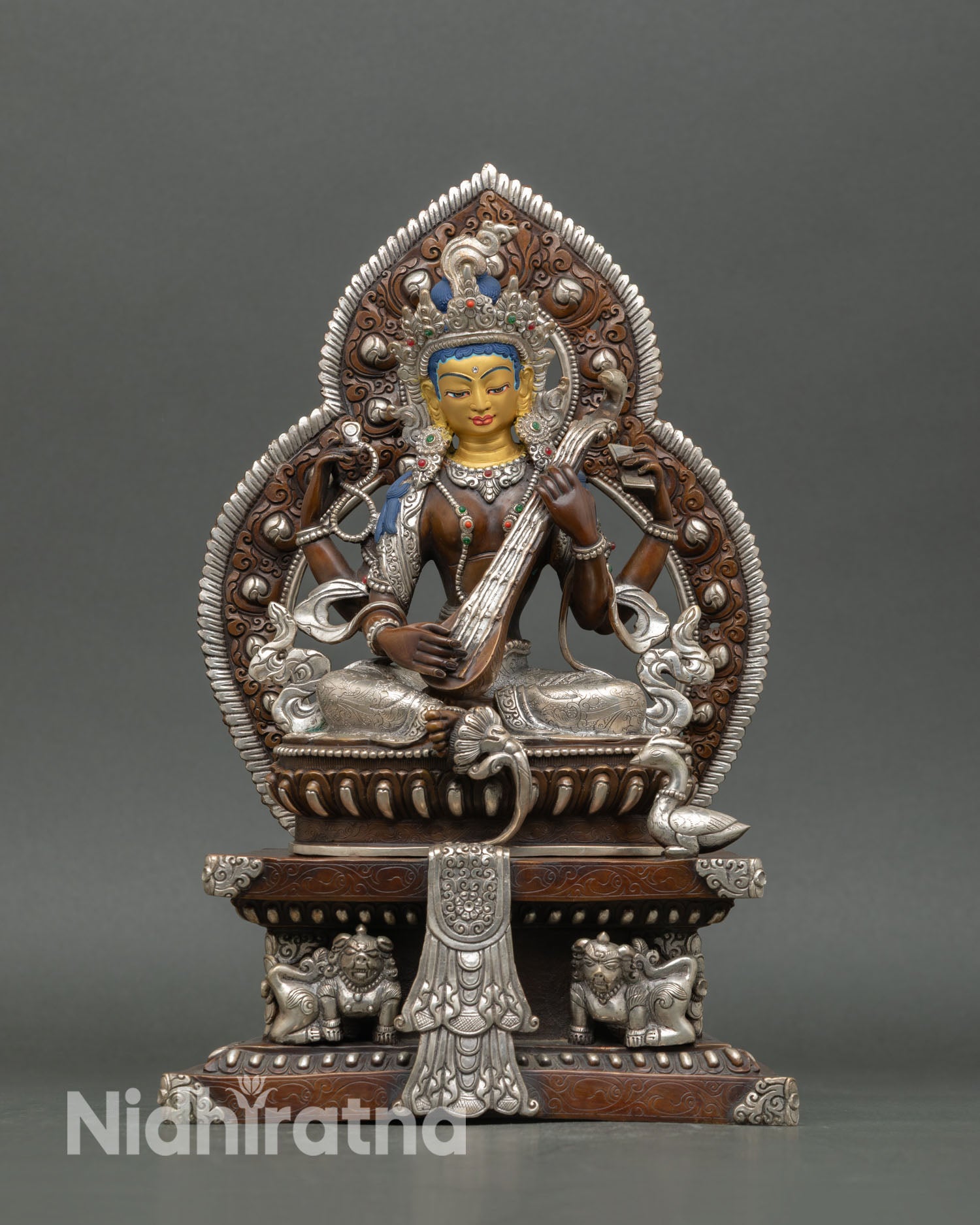 Front view of Saraswati statue handcrafted in Nepal with copper body, silver plated detailing, gold painted face, and ornate throne supported by snow lions