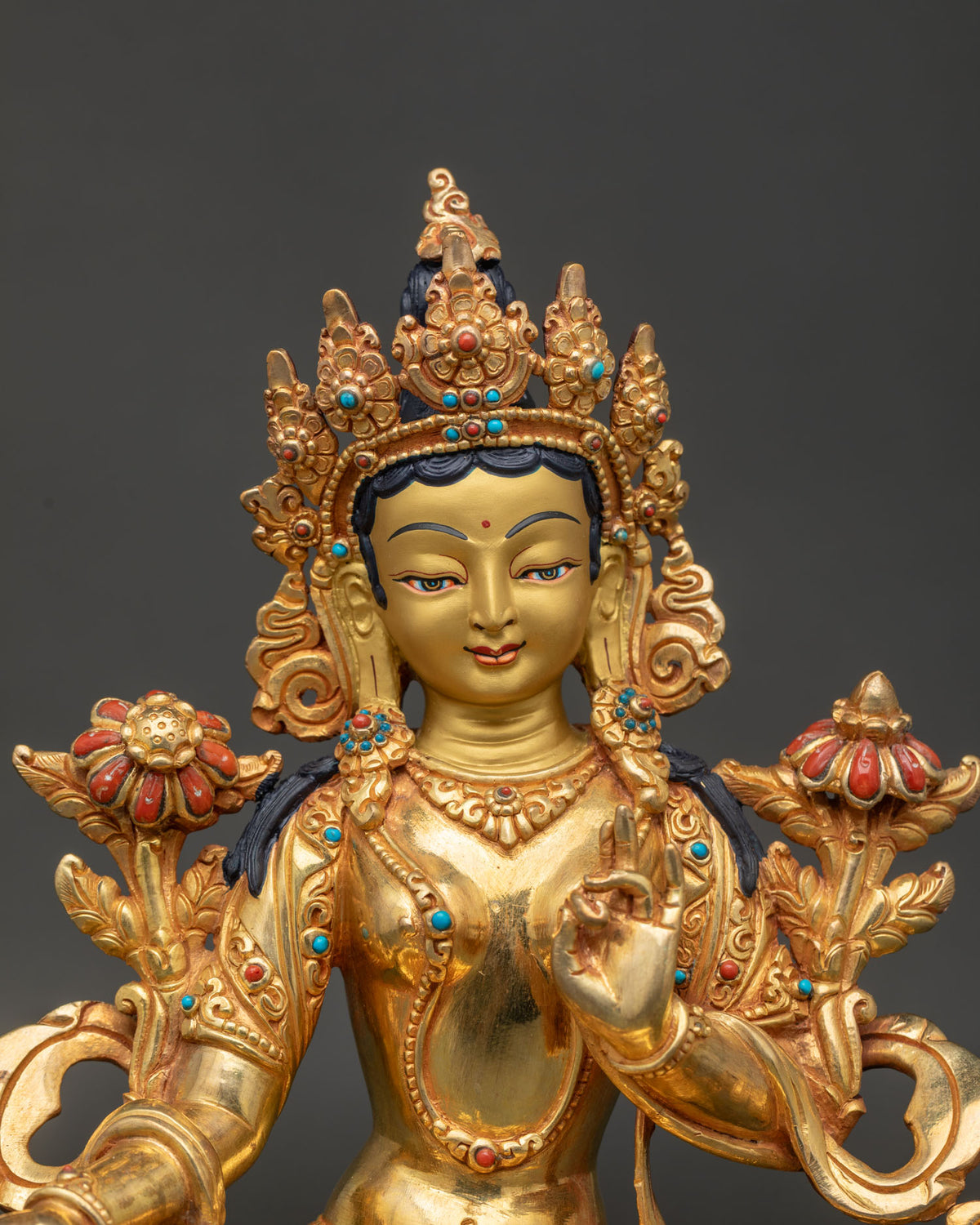 Green Tara statue close up showing peaceful 24K gold painted face five jeweled diadem and stone jewelry.