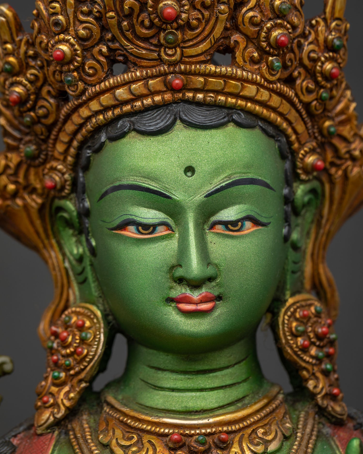 Green Tara statue face close-up, serene expression with five-jeweled crown