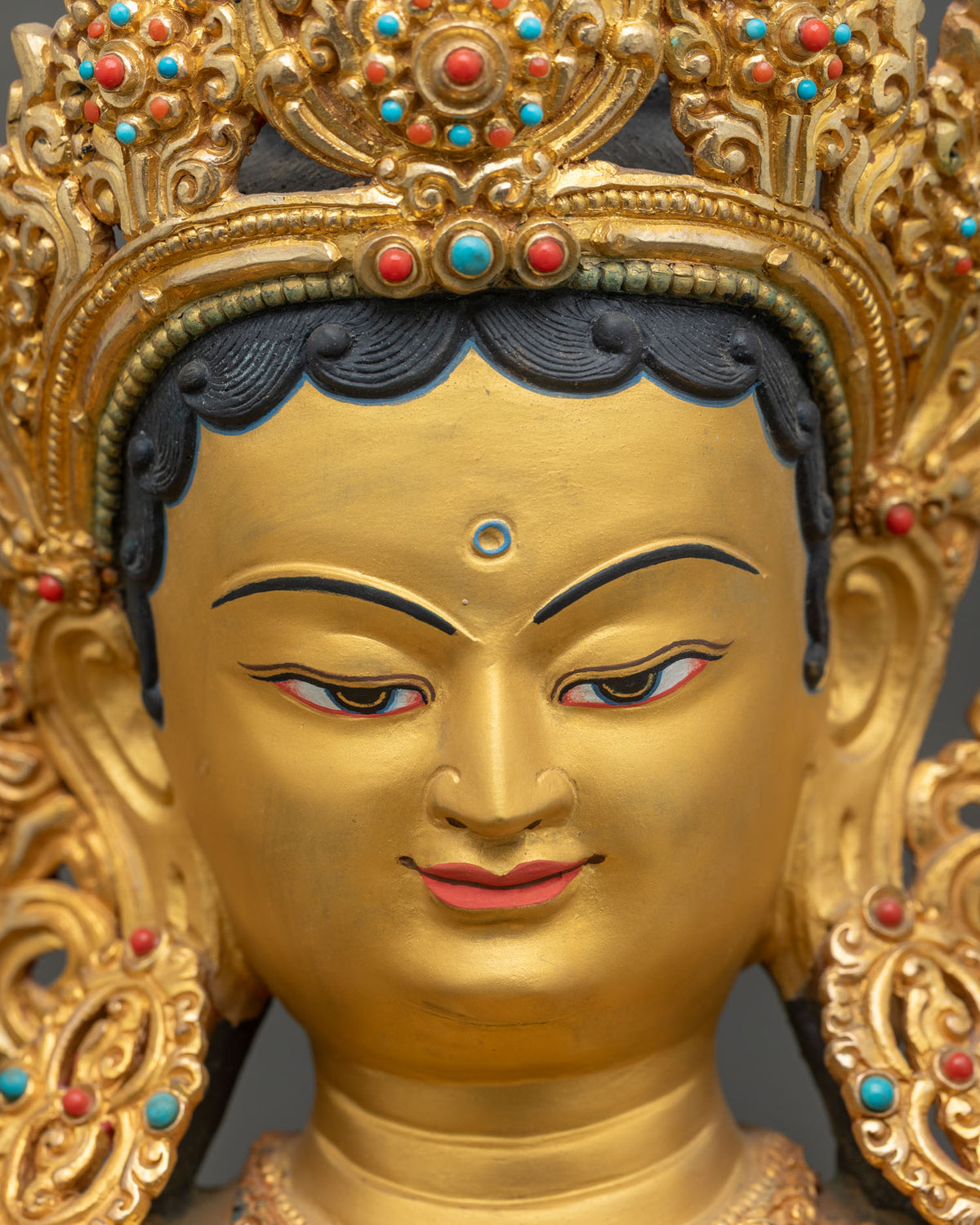 Green Tara statue face detail with gentle gold-painted features and jeweled crown