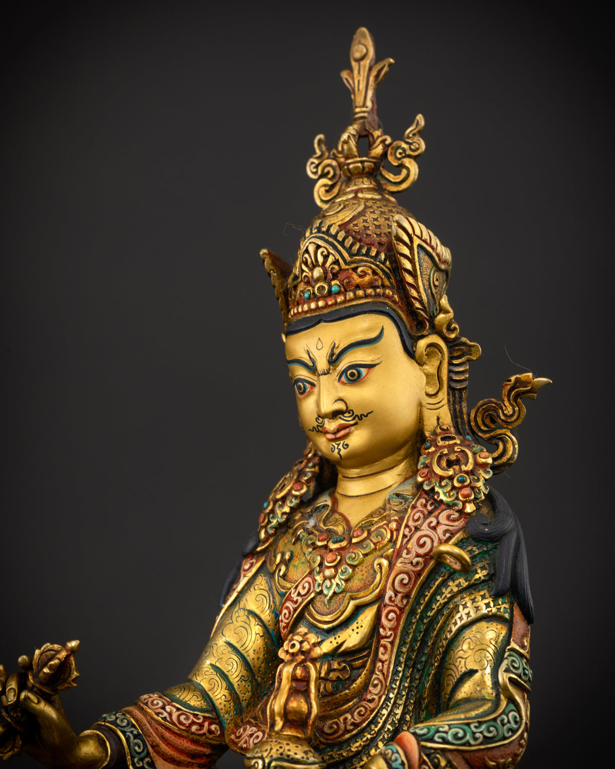 Guru Rinpoche statue wearing ceremonial robes with hand carved floral motifs and semi precious stones.