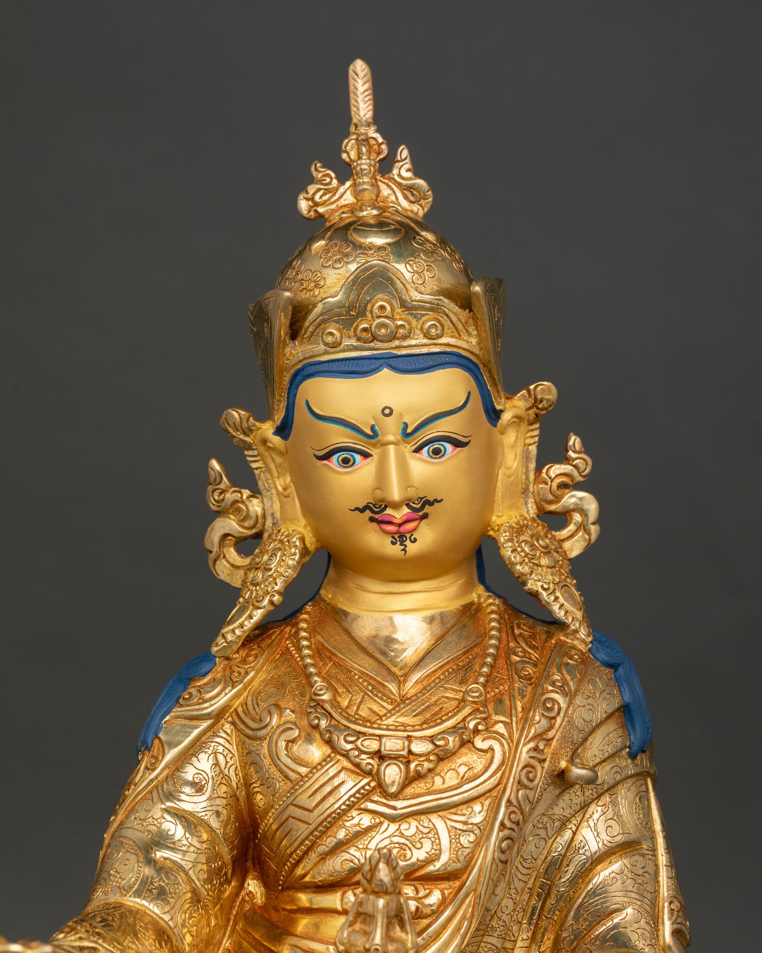 Guru Rinpoche statue close-up showing gold-gilded robes, sacred implements and gemstone details