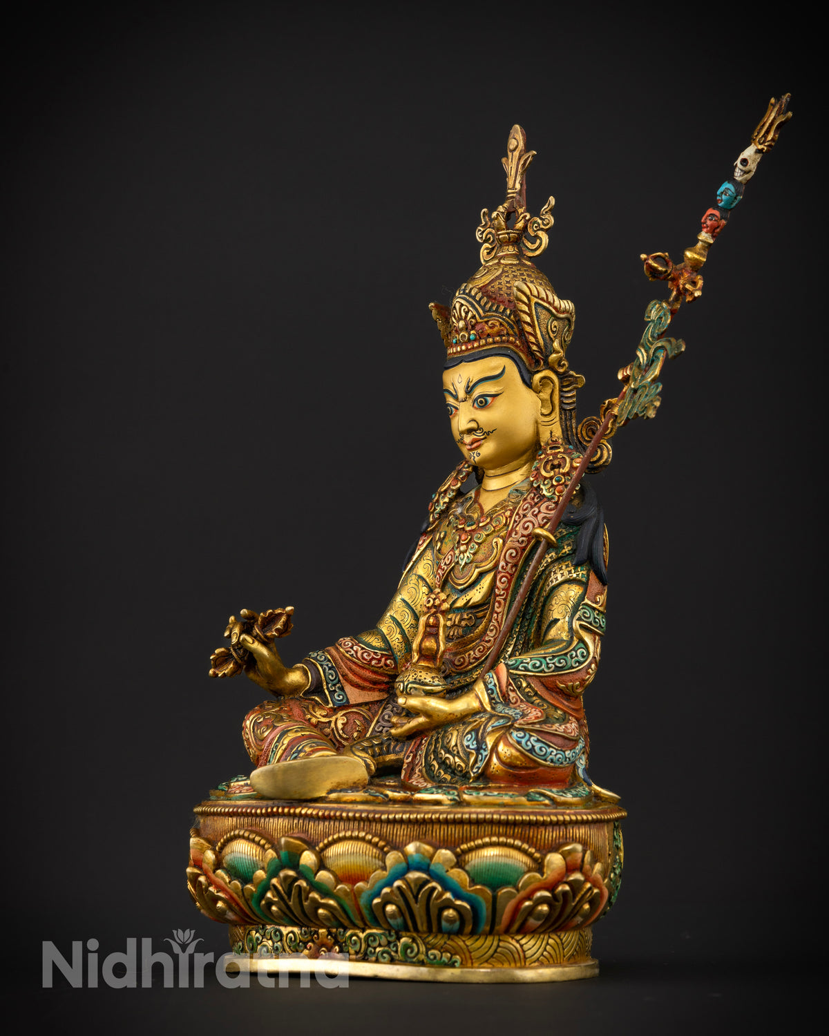 Guru Rinpoche statue with a khatvanga trident staff decorated with symbolic skulls and a flowing banner.