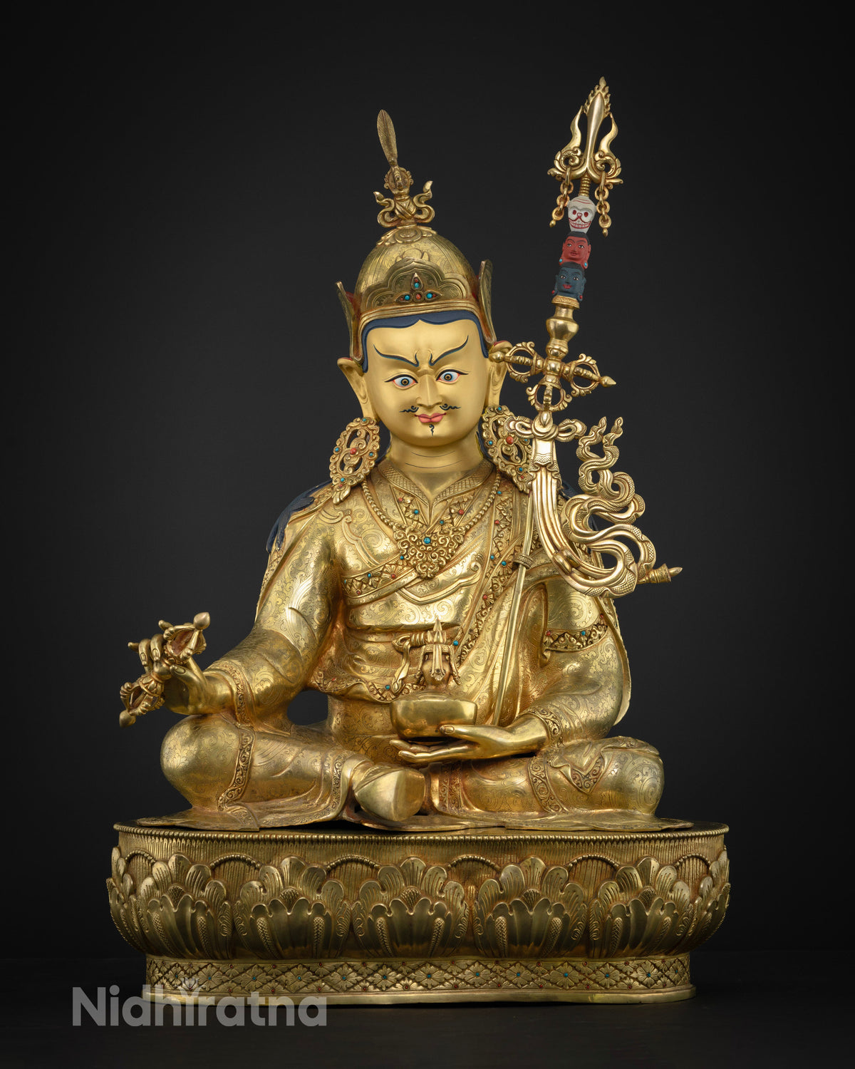 Guru Rinpoche statue seated on the lotus throne, holding vajra and skull cup, symbolizing wisdom and enlightenment in Tibetan Buddhism.