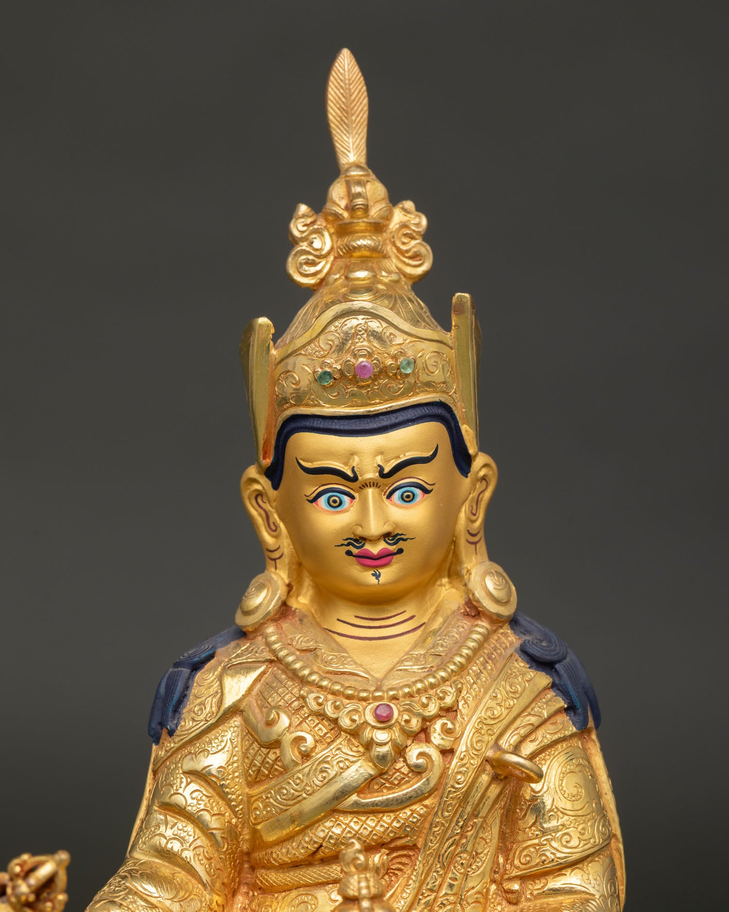 Guru rinpoche statue showing gold painted face and ornate crown details.