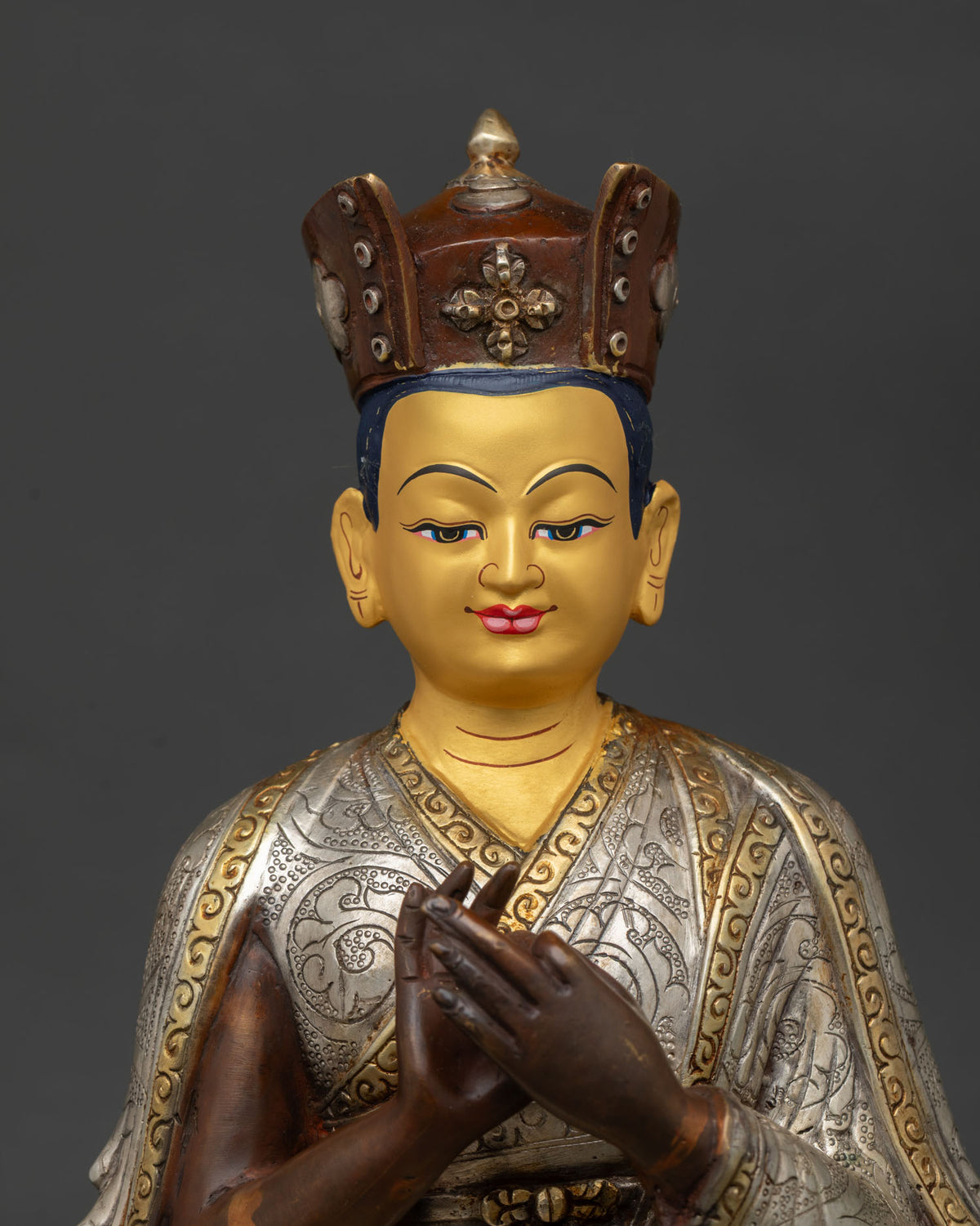 Karmapa statue seated on pedestal with black ritual crown and gold painted face.