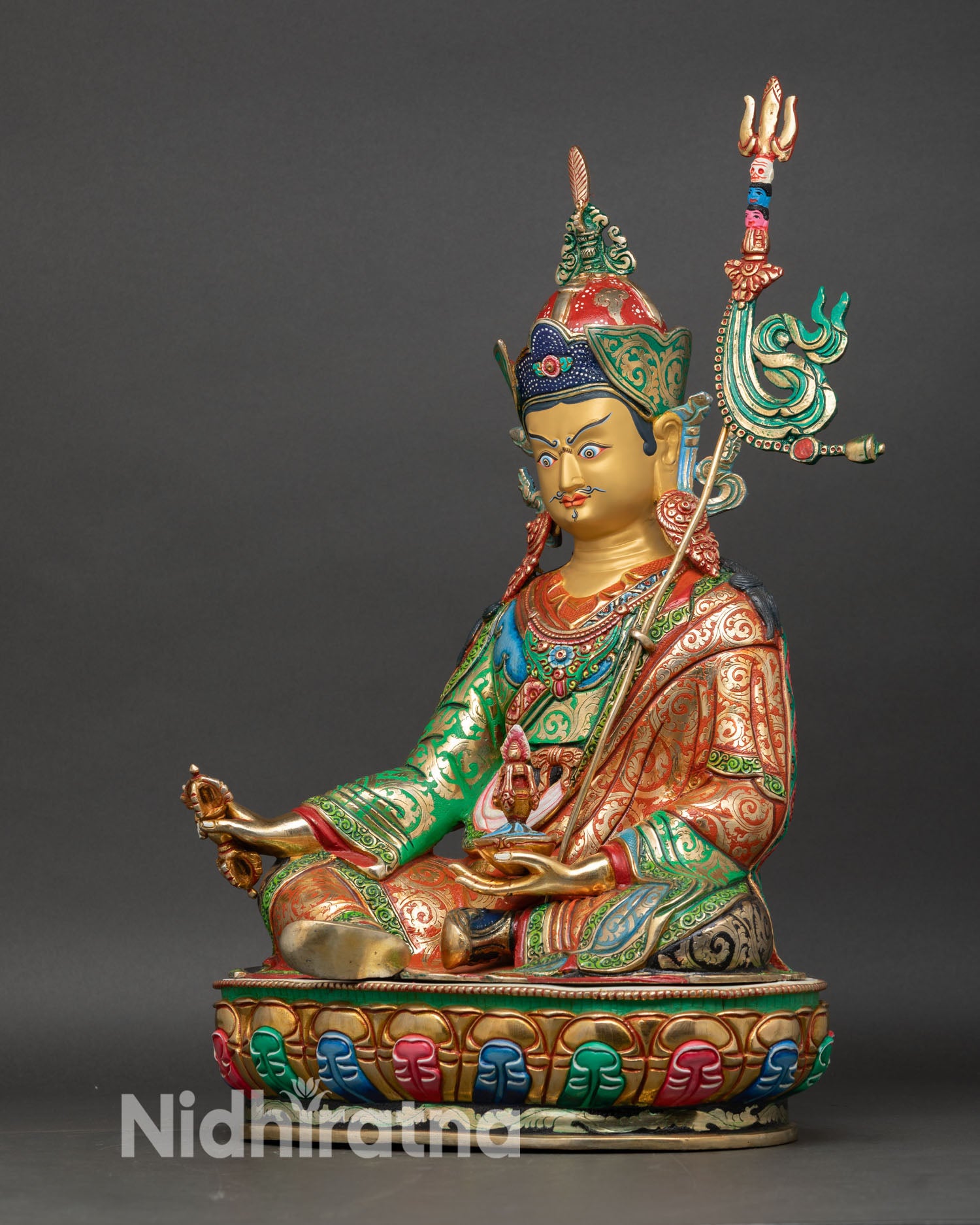 Left side view of Padmasambhava statue showing khatvanga trident, ornate robes, and gilded copper texture