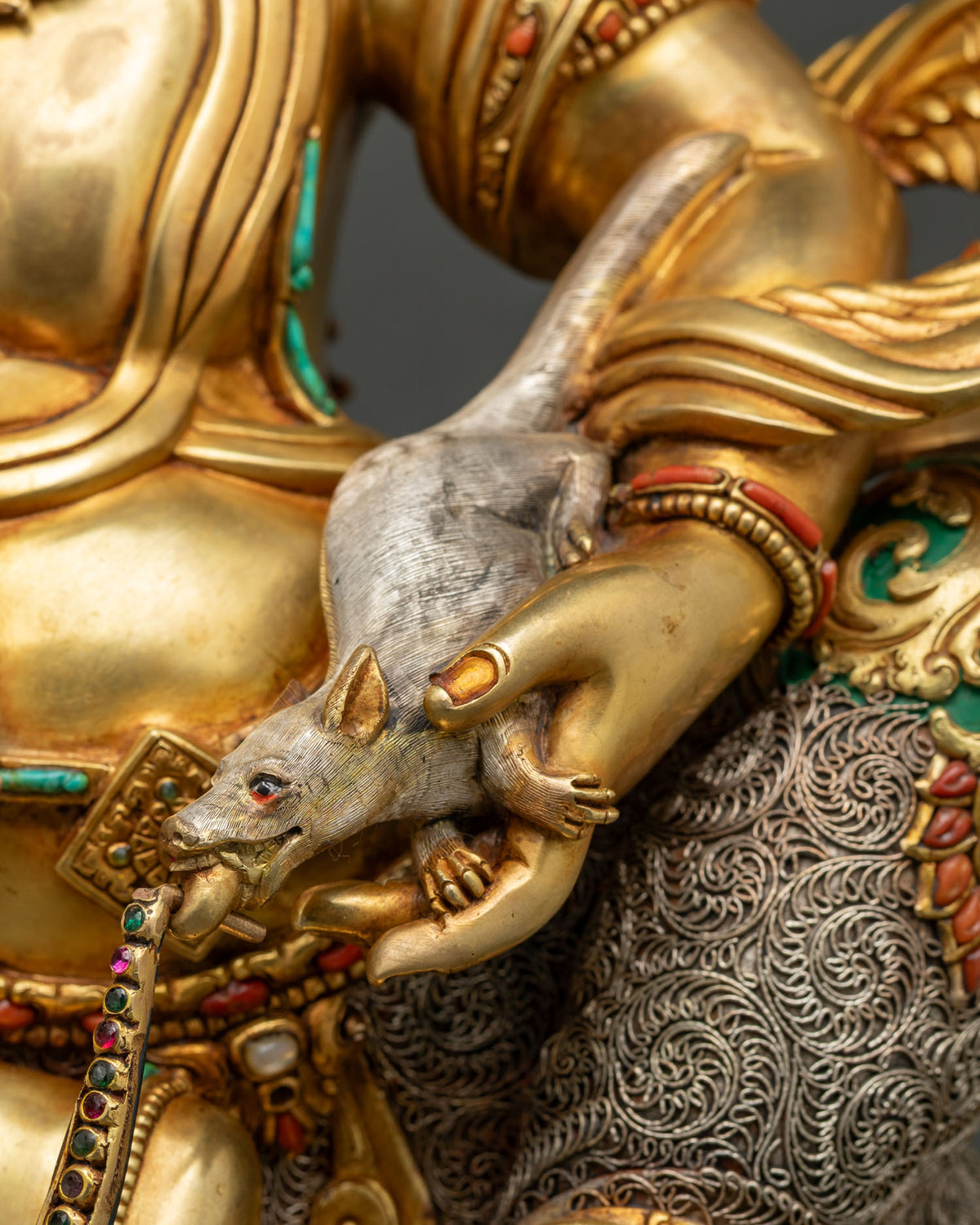 Namtoshe statue holding a silver jewel-spitting mongoose, symbol of wealth, beside filigree garment