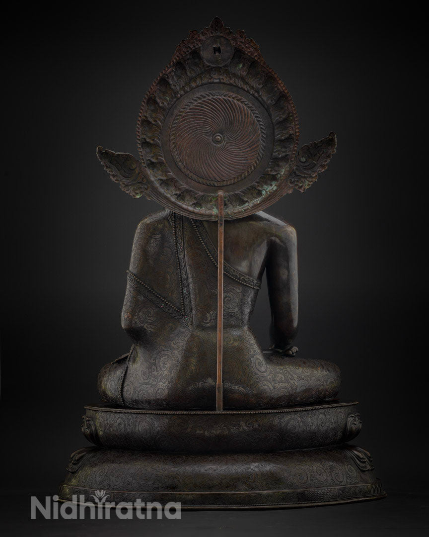 Back view of oxidized copper Buddha statue showing carved aureole and robe