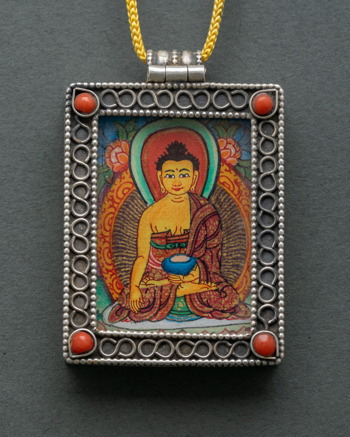 Shakyamuni Buddha locket made from silver with intricate filigree patterns and semi-precious coral stones.