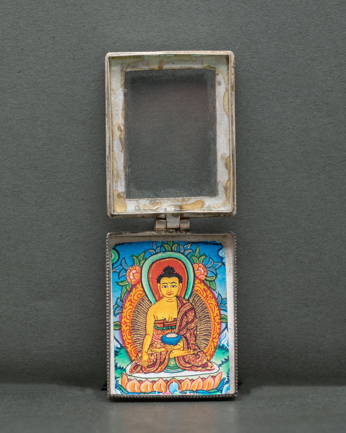Shakyamuni Buddha silver locket handcrafted by a skilled Newari artist from Patan, Nepal, with ornate filigree and coral stone accents.