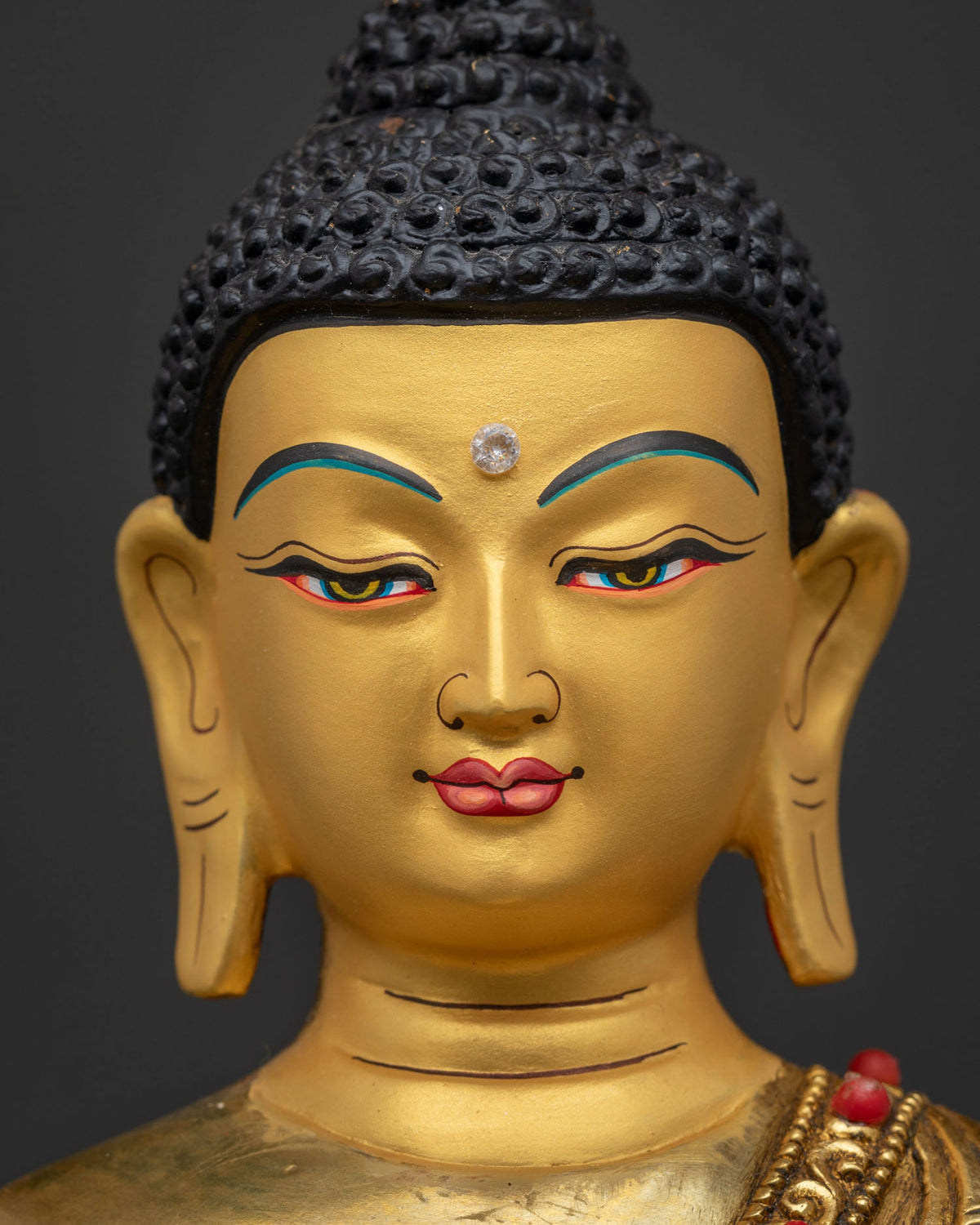 Shakyamuni Buddha statue close up showing 24k gold painted face semi precious stones and Bhumisparsha Mudra.