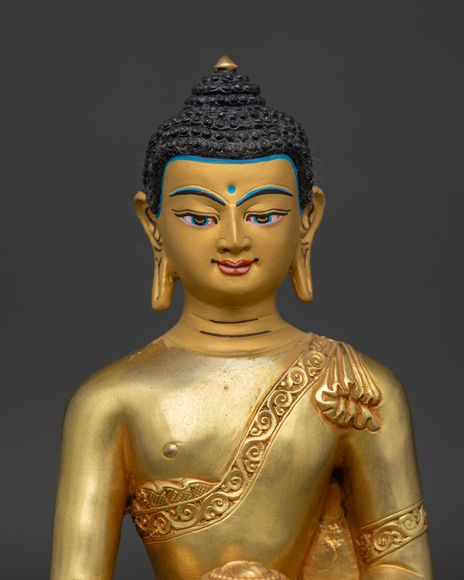 Shakyamuni Buddha statue close up showing gold painted face and hand carved monk robe.