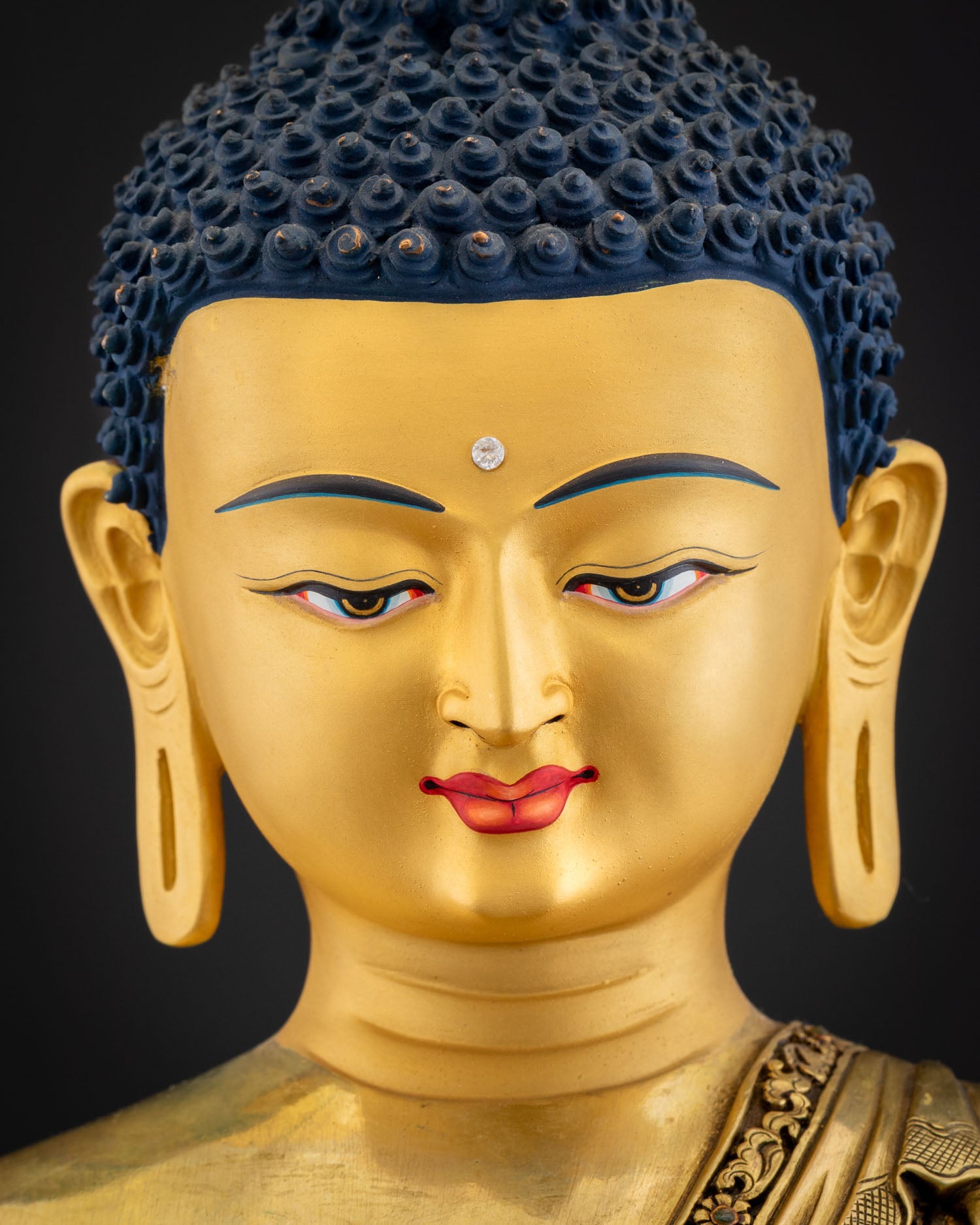 Shakyamuni Buddha statue face close-up showing Urna jewel, blue Ushnisha hair and half-closed eyes
