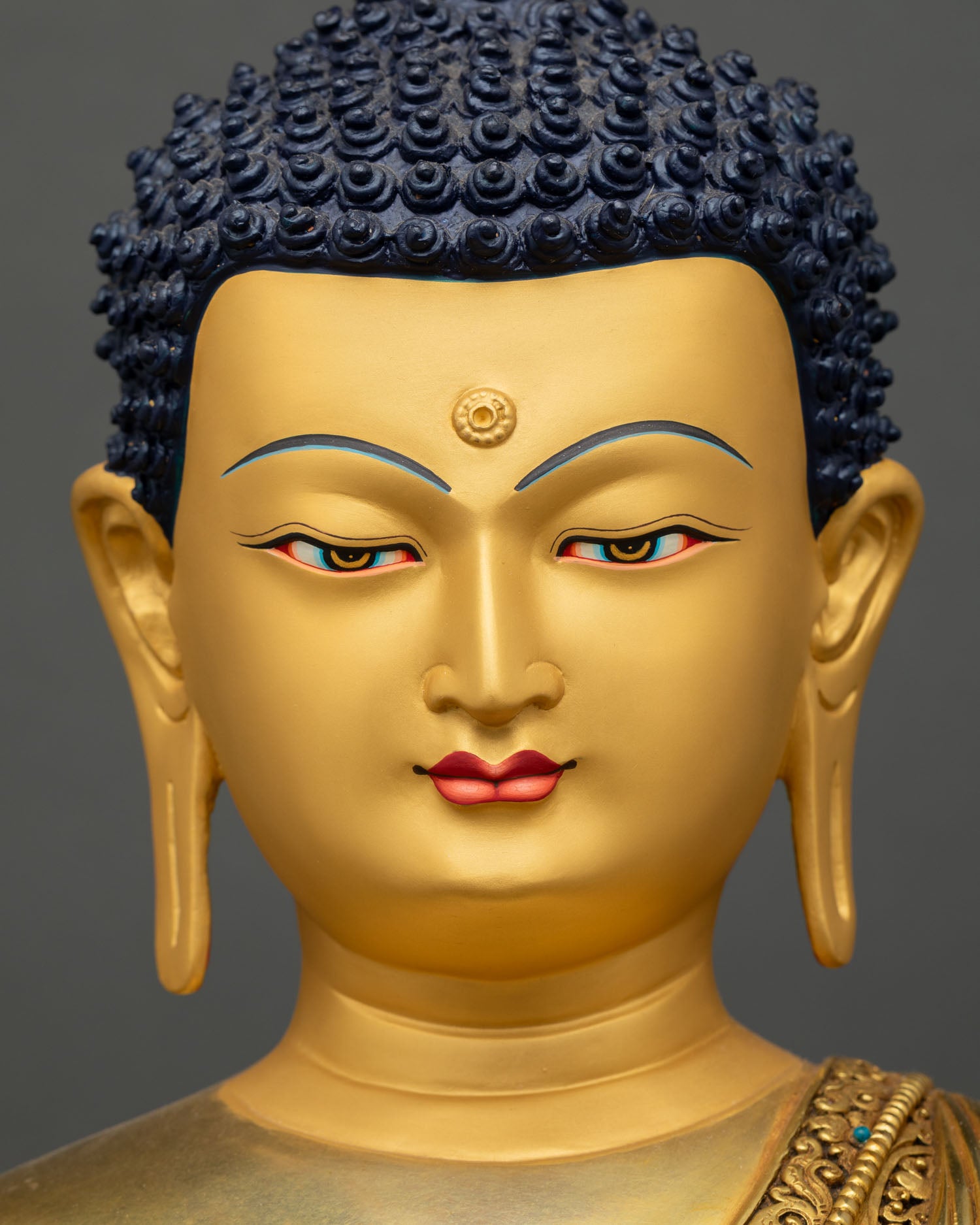 Shakyamuni buddha statue face detail with gold painted head and blue curled-hair