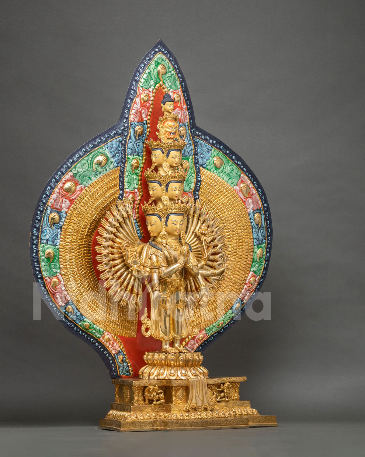 Side-angle view of 1000-armed Chenrezig statue on lotus base with painted gold backdrop