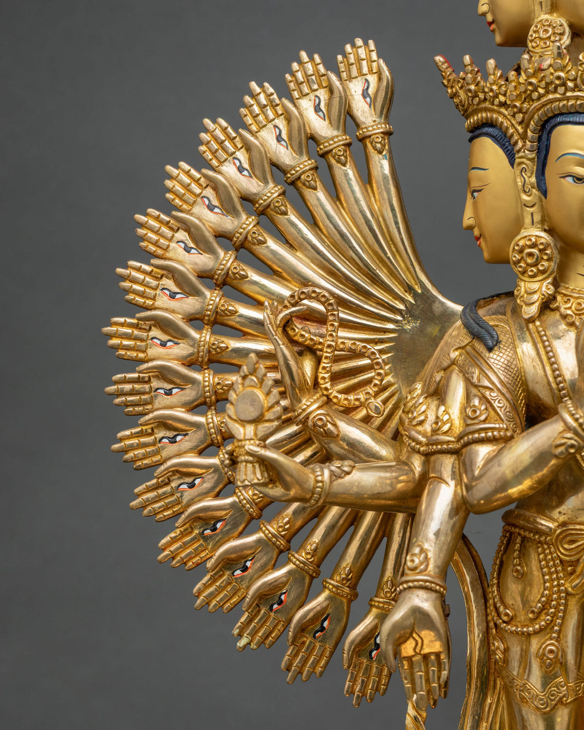 Side close-up of 1000-armed Chenrezig statue showing gold arms with an eye on each palm