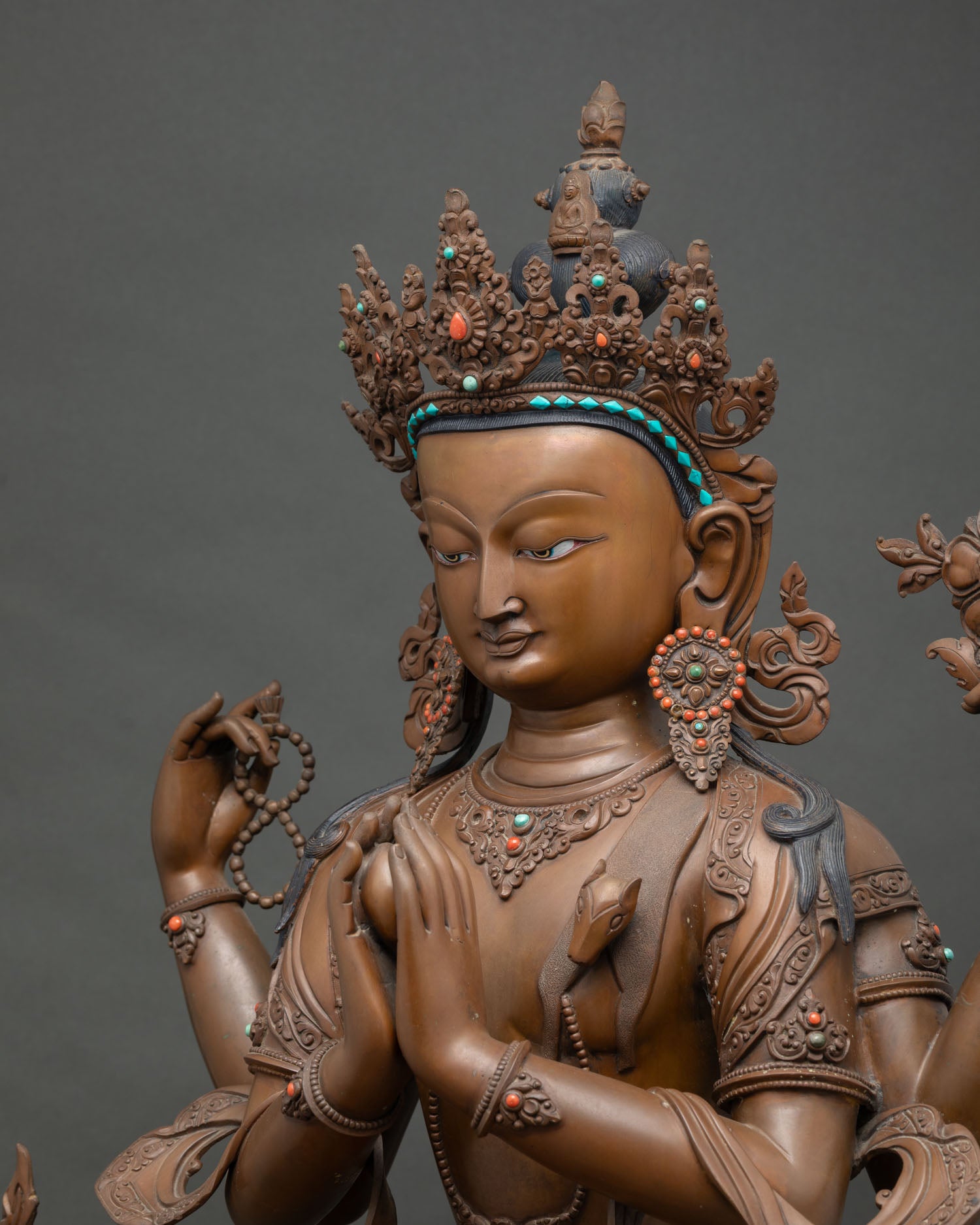 Side close-up of Chenrezig statue showing oxidized copper texture and coral inlay