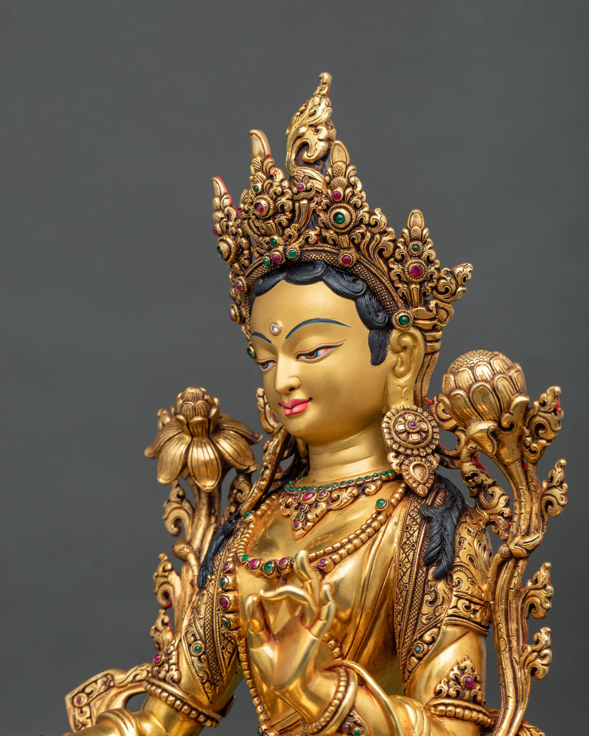Side close up of hand-carved gold gilded Green Tara statue with jeweled crown and lotus