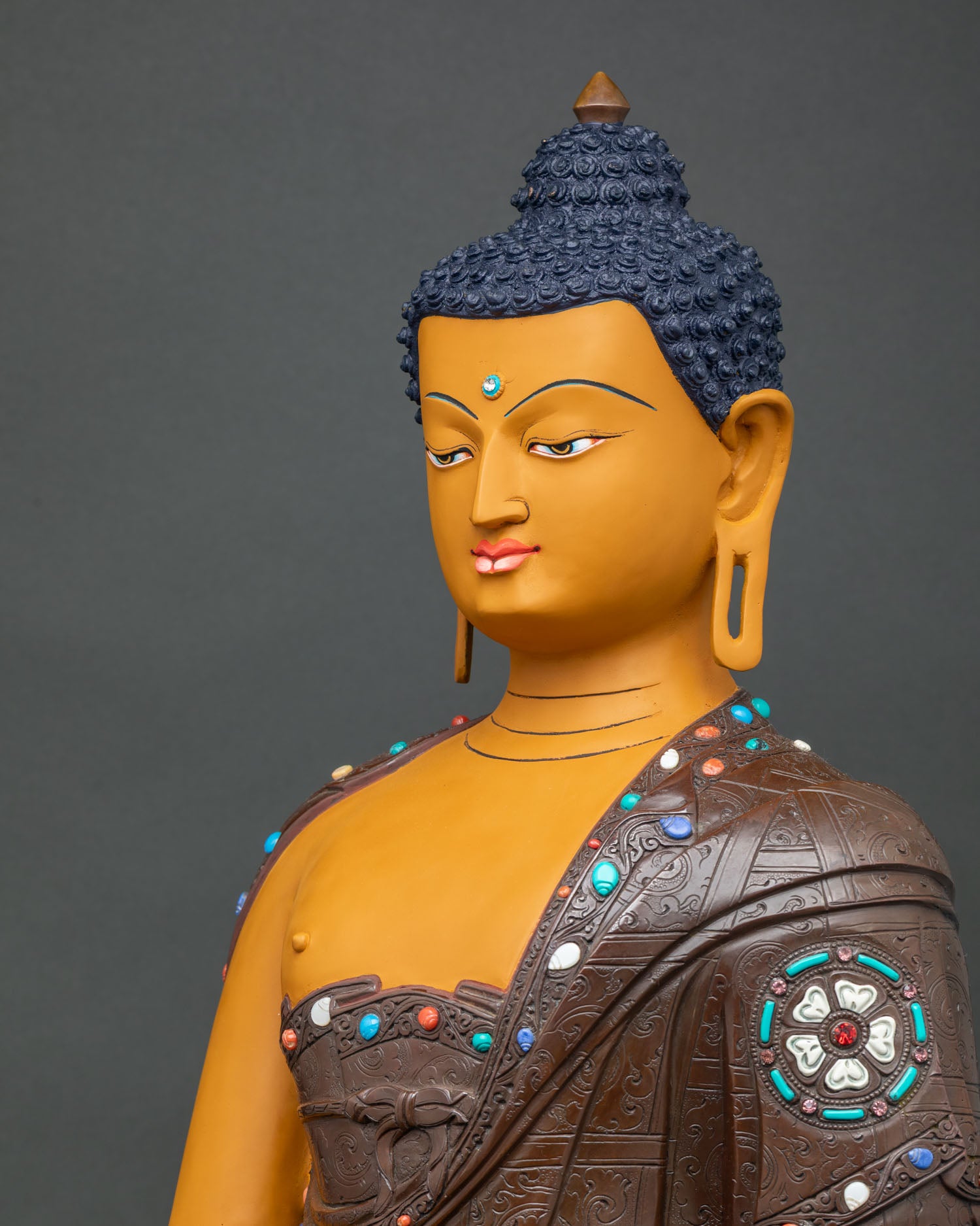 Side close-up of Shakyamuni Buddha statue showing engraved robe, stone inlays and lotus pedestal