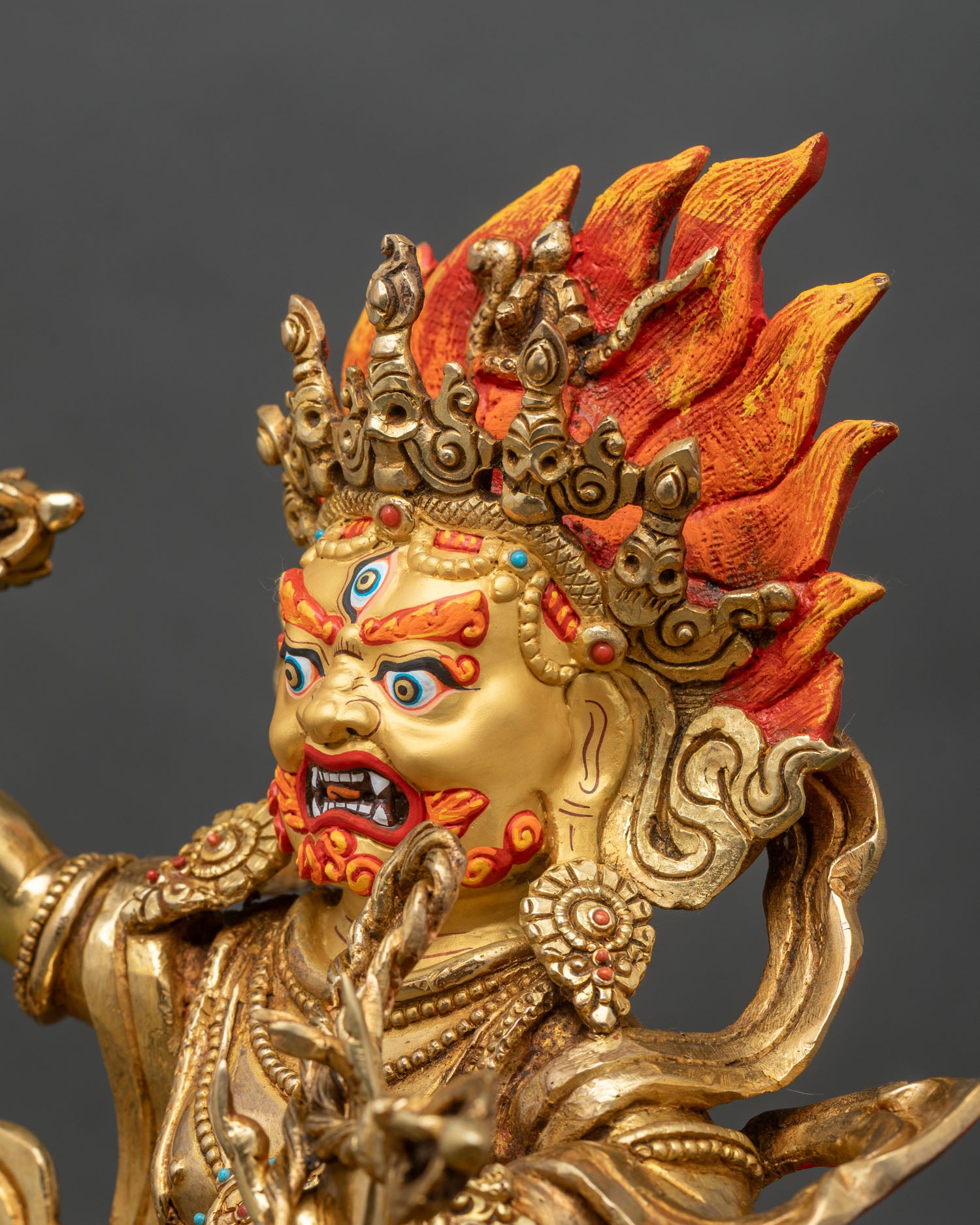 Side close up of Vajrapani statue highlighting arm movement, vajra and flame backdrop
