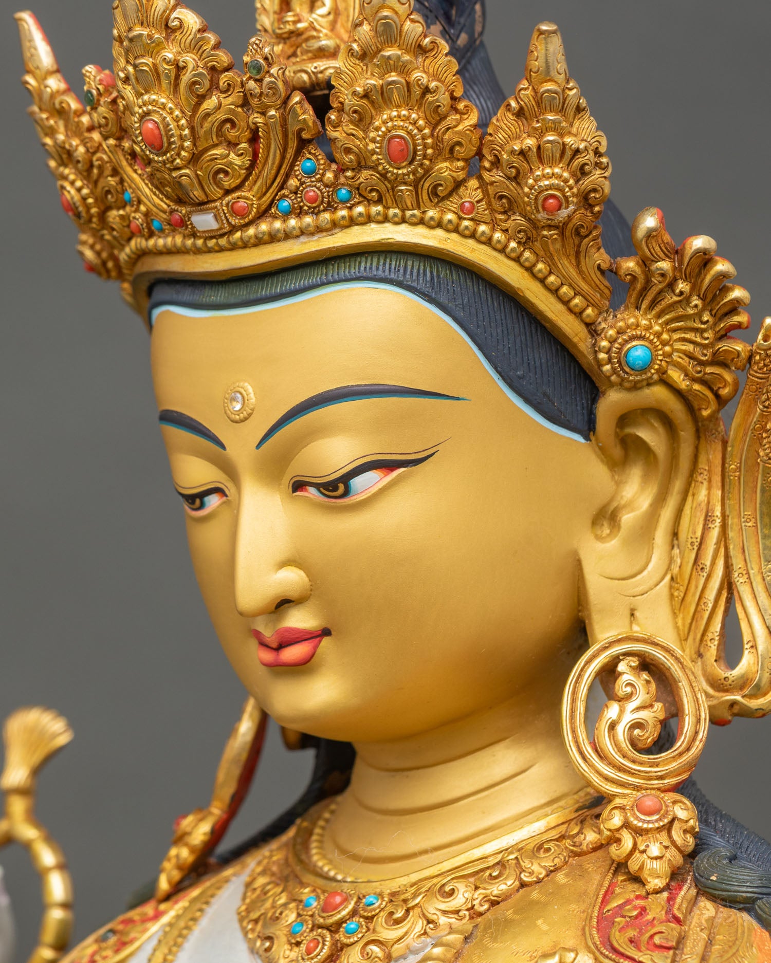 Side face close up of Chenrezig statue with crown, turquoise stones, and compassionate gaze