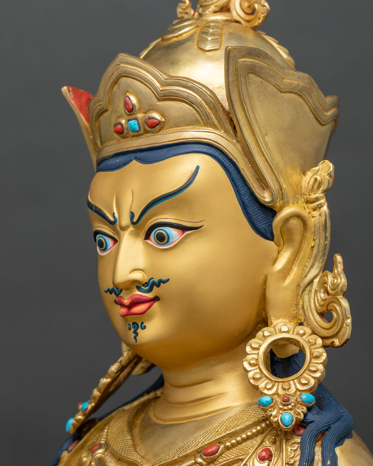Side profile close up of Guru Rinpoche statue face, gold-painted with mustache and lotus hat