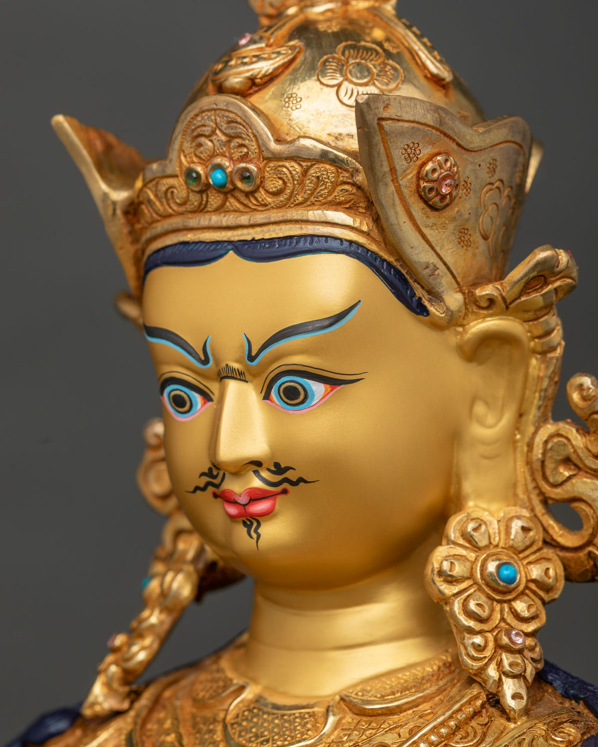 Side profile close up of Guru Rinpoche statue face with crown and gold detailing