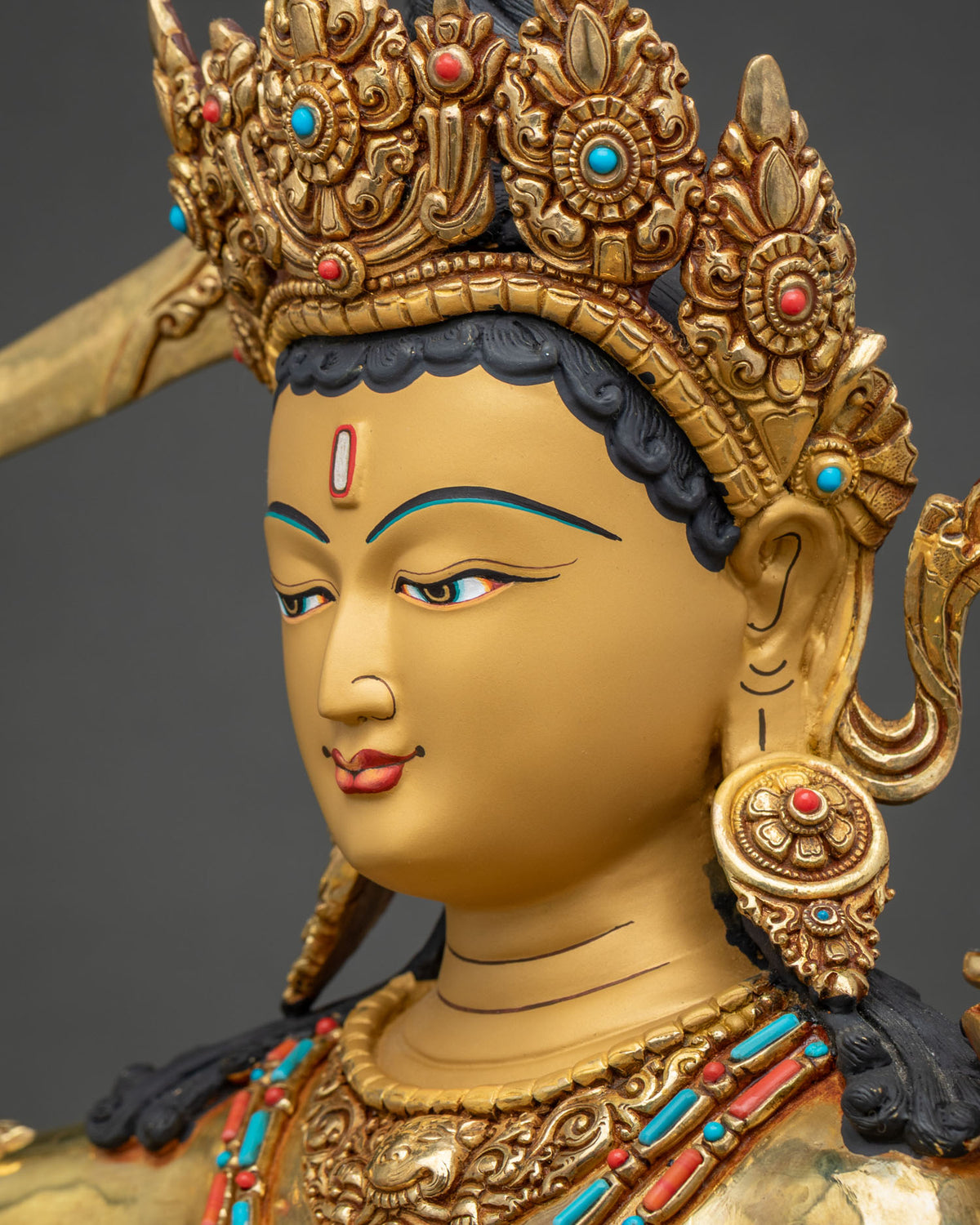 Side profile close-up of Maha Manjushri statue face with hand-painted eyes and gold jeweled crown