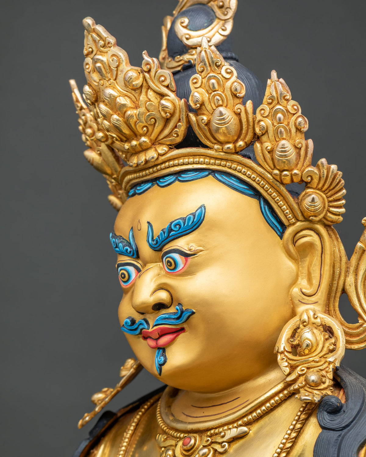 Side profile close up of Yellow Dzambhala face displaying gold diadem and hand painted details.