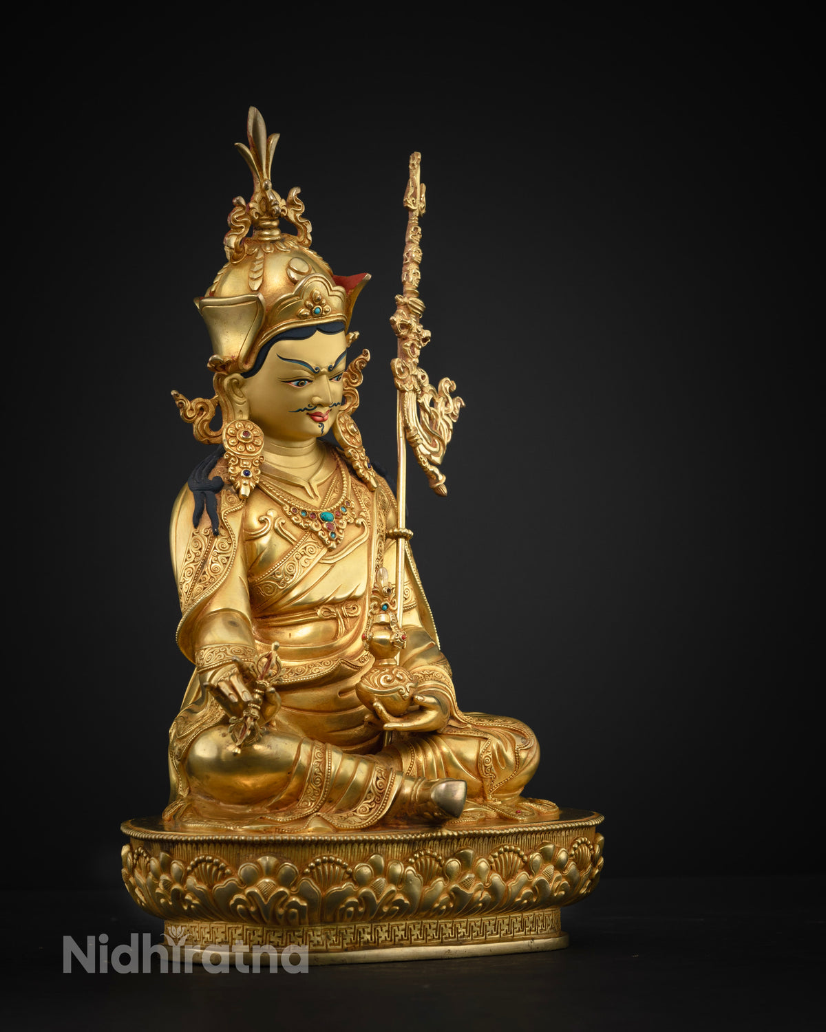 Side profile of gold-gilded Guru Rinpoche statue with ornate robes, staff, and detailed crown