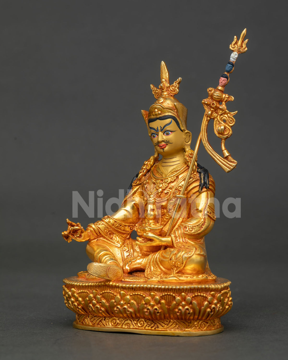 Side profile of gold Padmasambhava statue with raised khatvanga staff on lotus pedestal