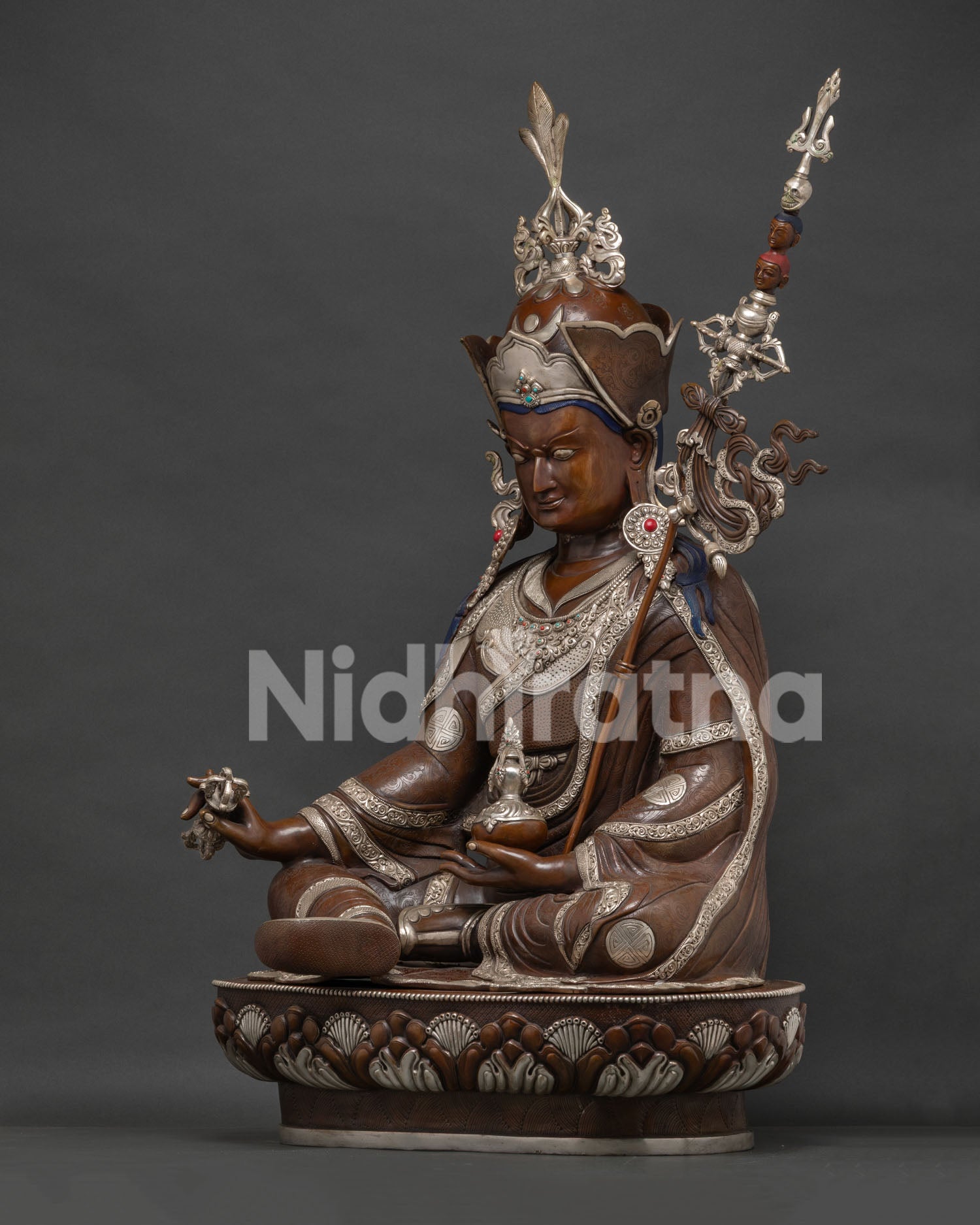 Side profile of Guru Rinpoche statue holding vajra, skull cup, and khatvanga staff.