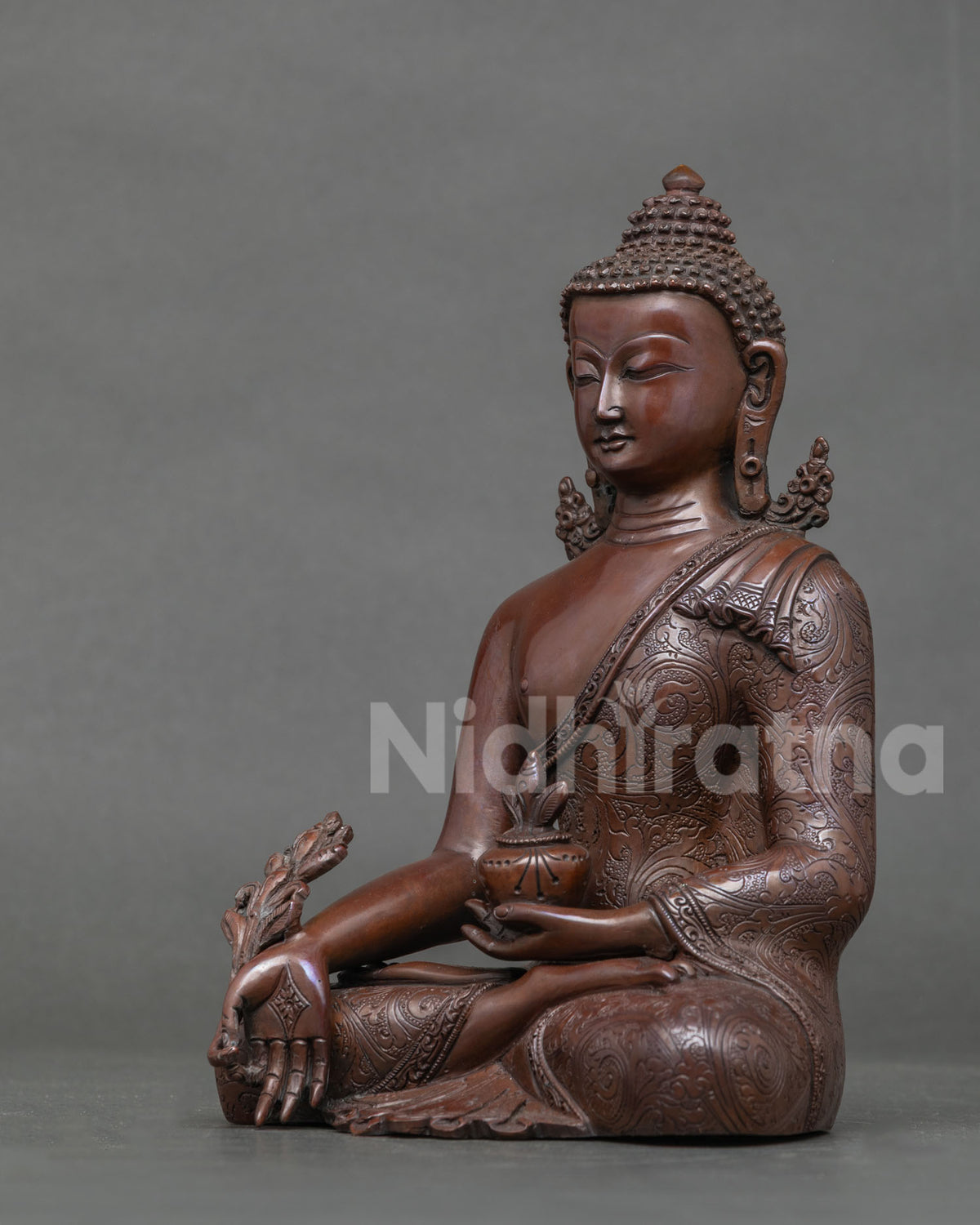 Side profile of oxidized copper Medicine Buddha statue seated with medicine bowl
